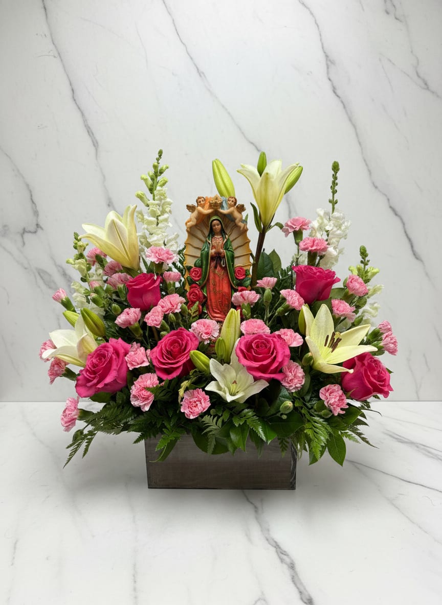 Pink roses and lilies arranged around a religious figurine in a rectangular vase