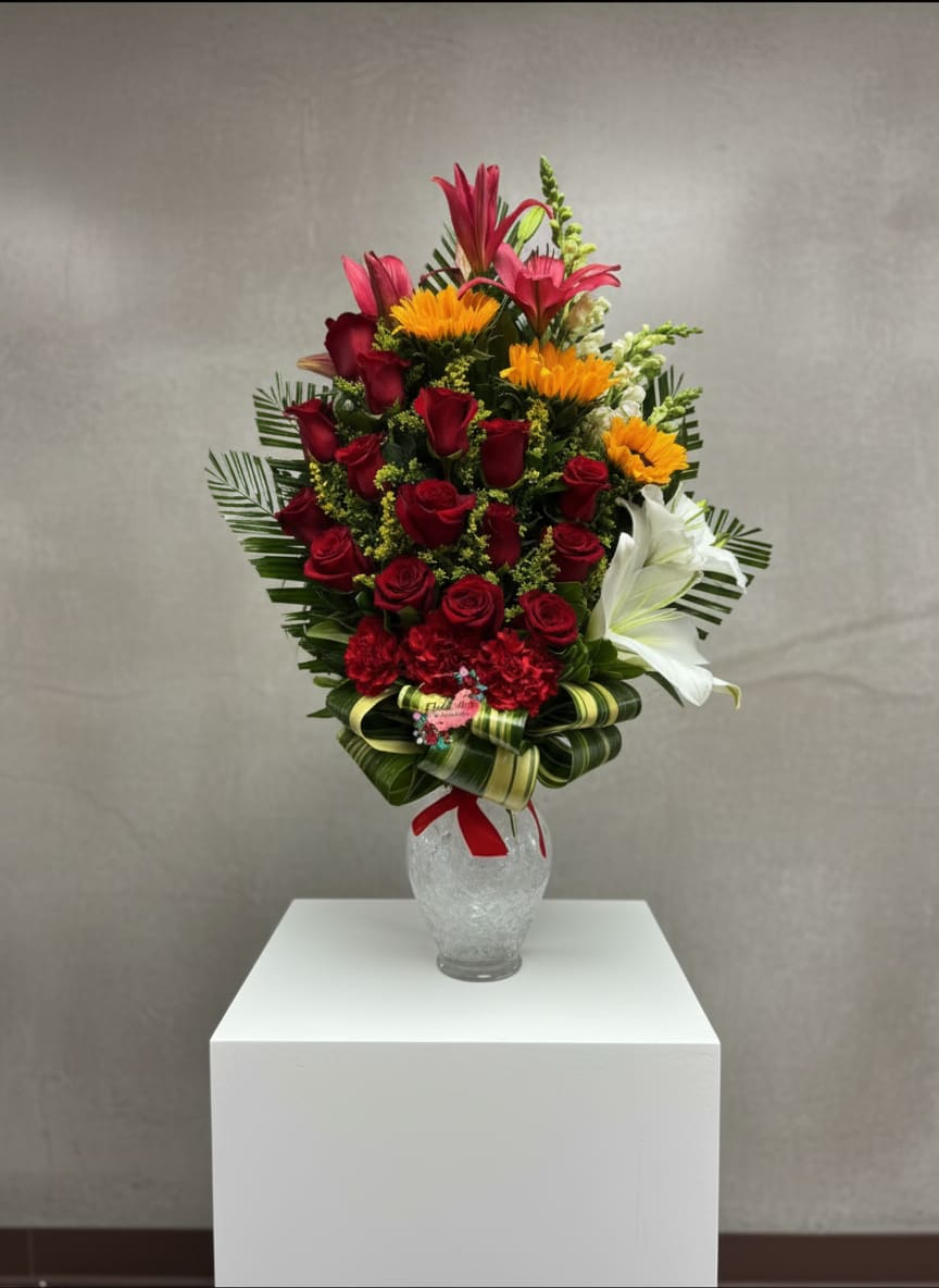 Tall bouquet of red roses, lilies, and yellow flowers in a glass vase
