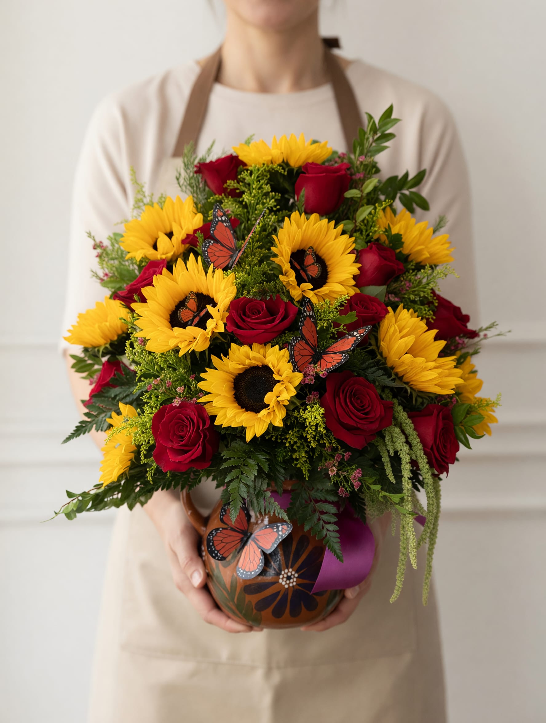 Martina  - Arreglo Floral Especial para Mamá ️    Celebra el amor más puro con este hermoso arreglo que combina la alegría de los girasoles con la elegancia de las rosas rojas. Cada flor ha sido cuidadosamente seleccionada para transmitir cariño, gratitud y admiración, creando una composición llena de vida y color.    Las delicadas mariposas decorativas añaden un toque único y simbólico, representando el amor eterno, la transformación y la belleza de mamá en cada etapa de la vida. Acompañado de follaje fresco y presentado en una base artesanal, este diseño destaca por su estilo cálido, natural y sofisticado.    Un detalle perfecto para sorprender en el Día de las Madres, expresar todo lo que a veces no se dice con palabras y hacerla sentir verdaderamente especial. 