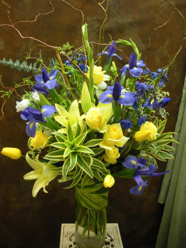 Blue irises and yellow roses in a tall glass vase