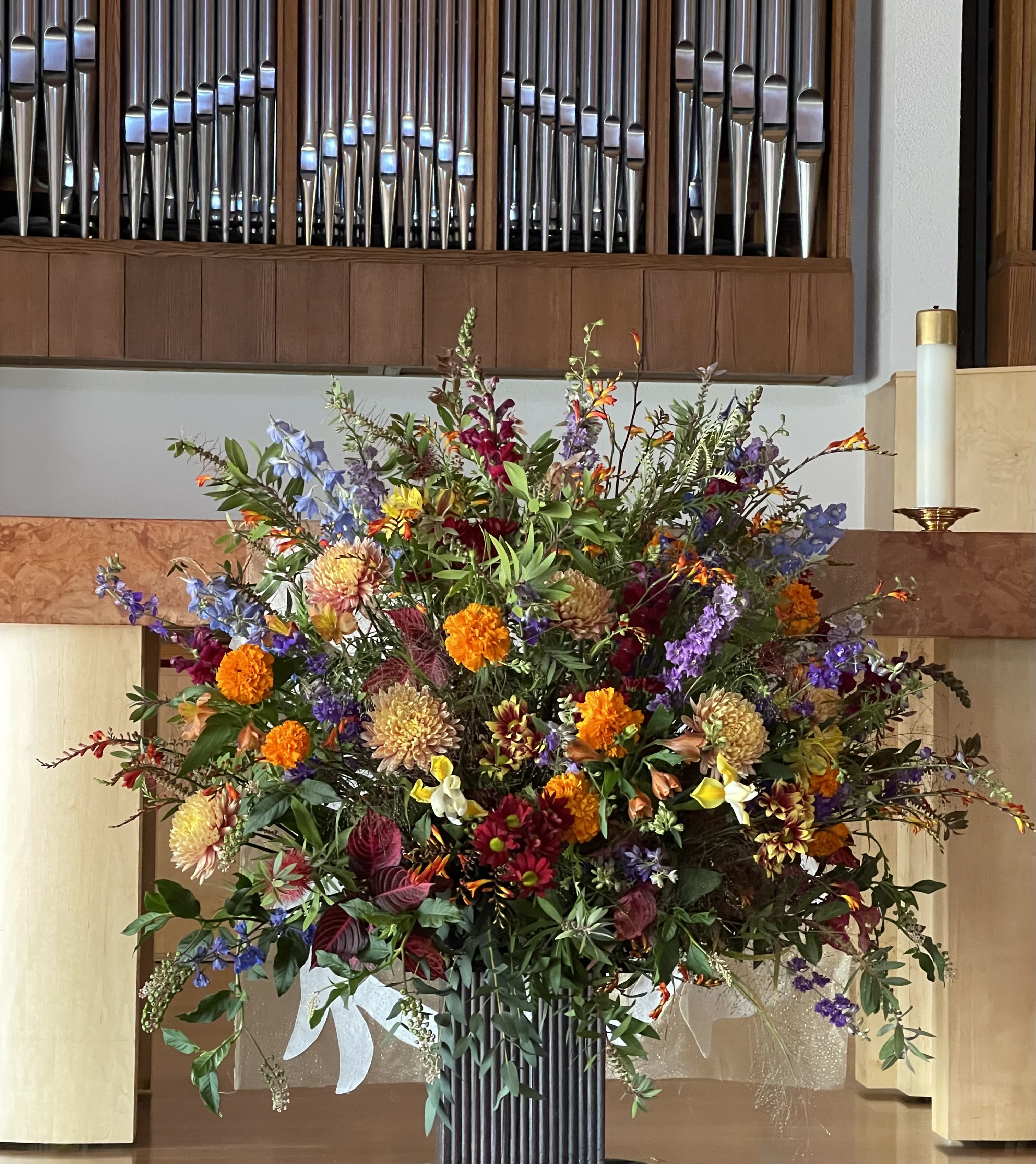 Large mixed floral arrangement in a tall vase with orange, purple, red, and white blooms