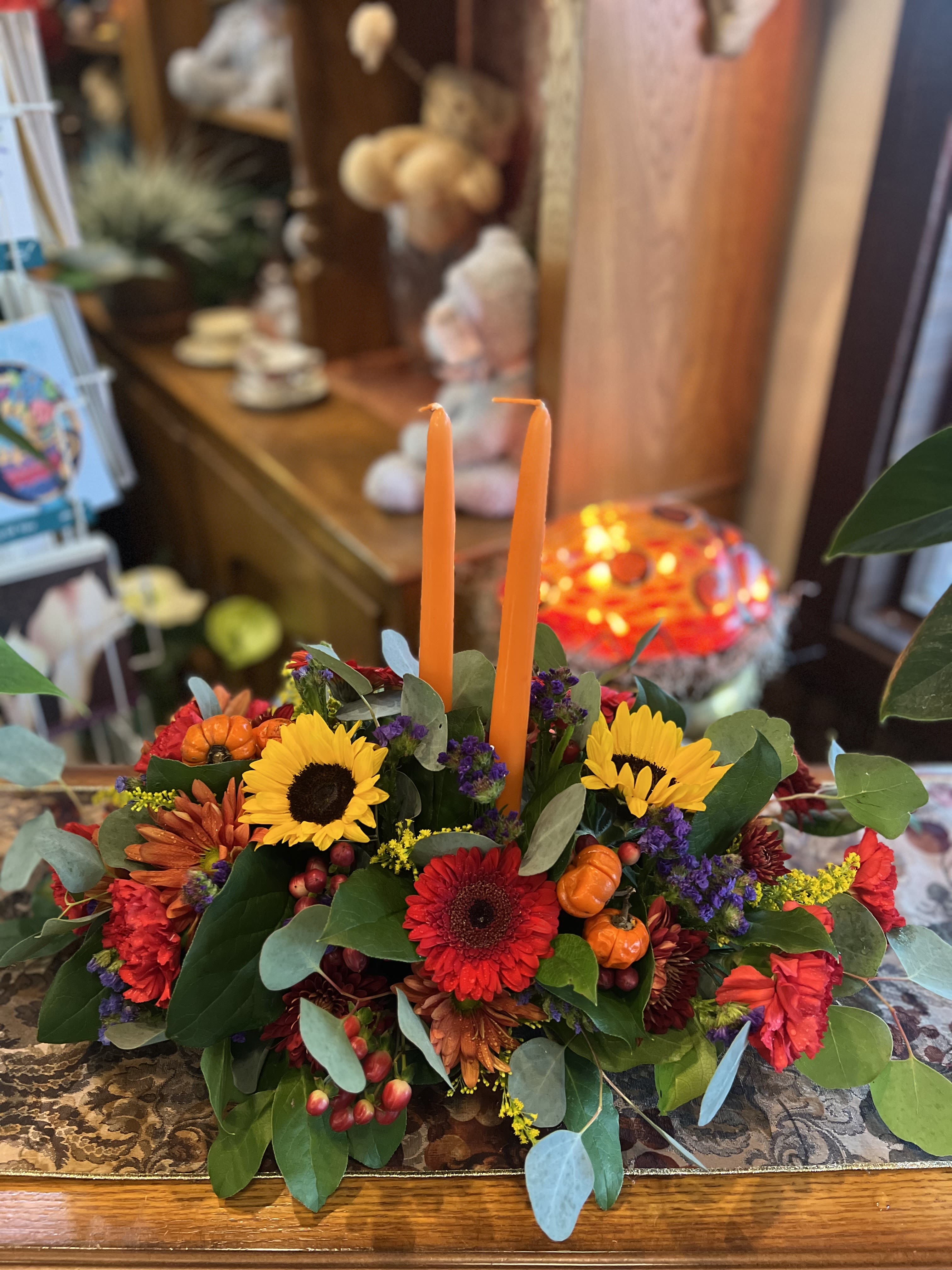 Thankful Blessings Centerpiece - An assortment of warm fall blooms perfect to garnish your table during this season of gathering. Sunflowers and red gerber daisies accompanied with purple statice, solid aster, red hypericum berries, and more!