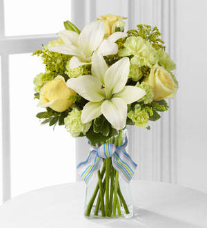 White lilies and pale yellow roses in a clear glass vase with a striped ribbon.