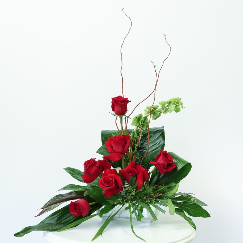 Red roses arranged in a clear glass vase with tall curly branches