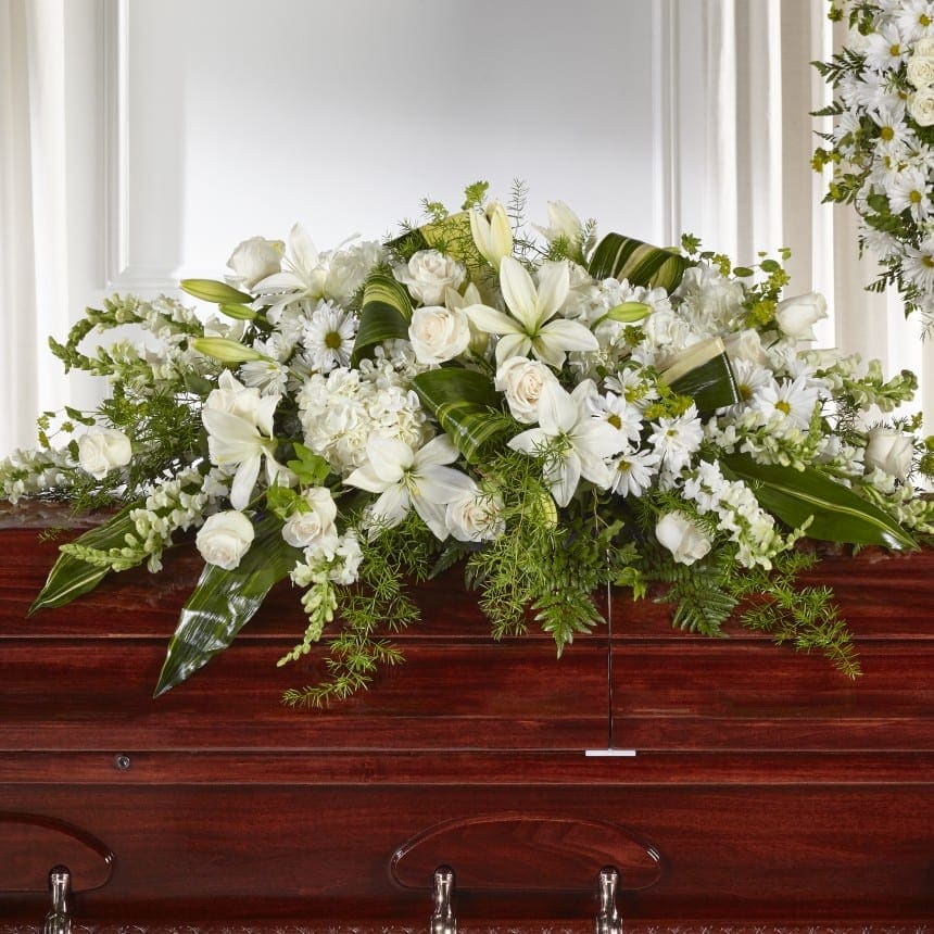 White floral casket spray with lilies, roses, and daisies