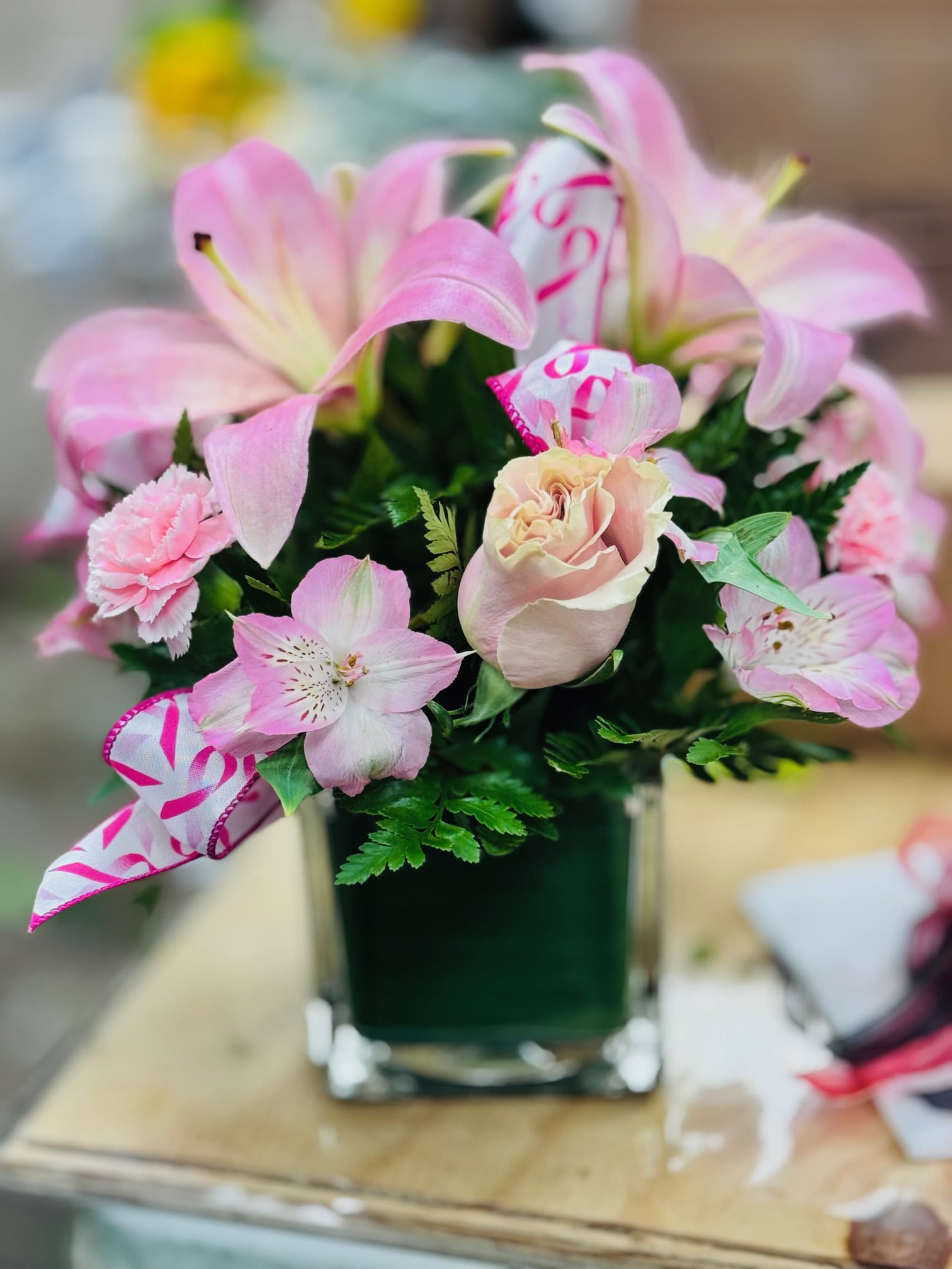 Pink lilies and roses arranged in a square glass vase