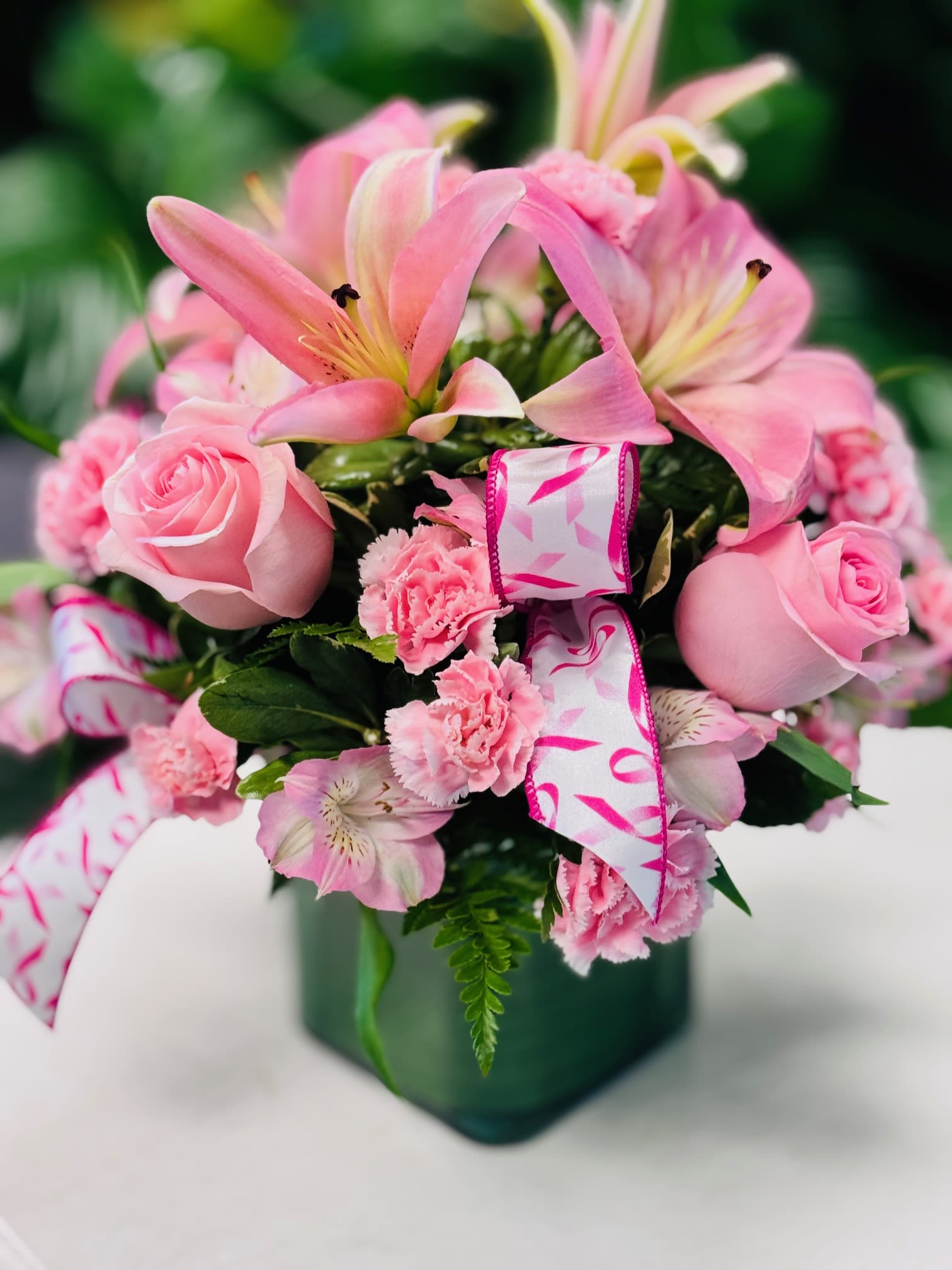 Pink lilies, roses, and carnations in a green vase with ribbon