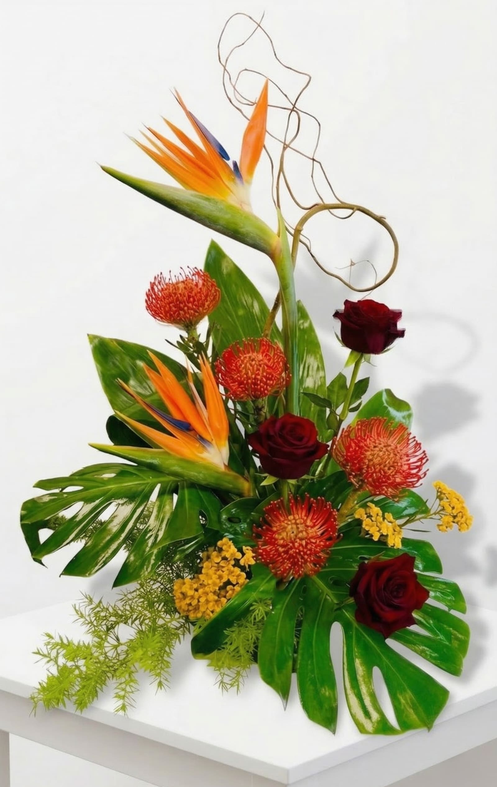 Tall tropical arrangement with bird of paradise, red roses, orange protea and yellow blooms on large glossy leaves