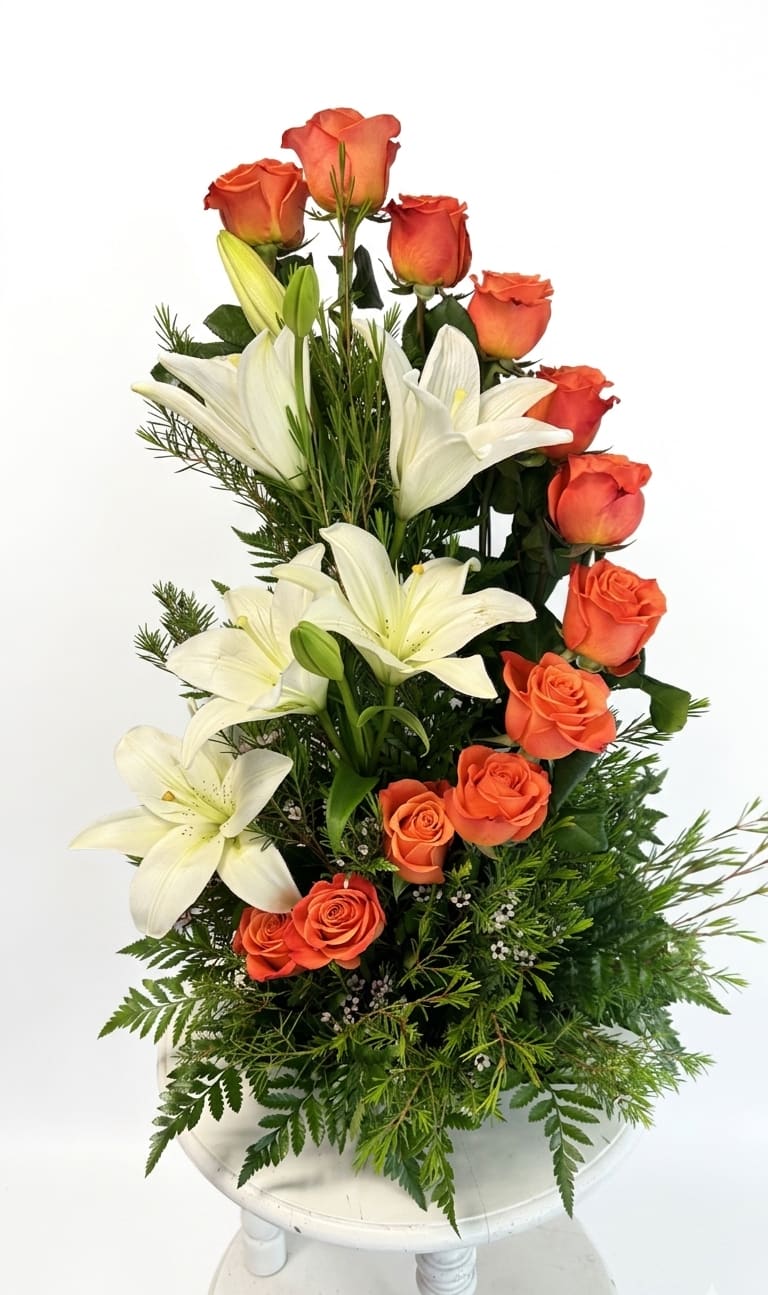 Tangerine Dream - A masterclass in floral architecture. Like a dreamy sunset dipping below the horizon, a brilliant cascade of orange roses sweeps gracefully down a structural backdrop of majestic white lilies and lush green foliage. Designed with a distinct one-sided presentation, this premium arrangement is crafted to bring dramatic height, texture, and sophisticated color to your home or office.