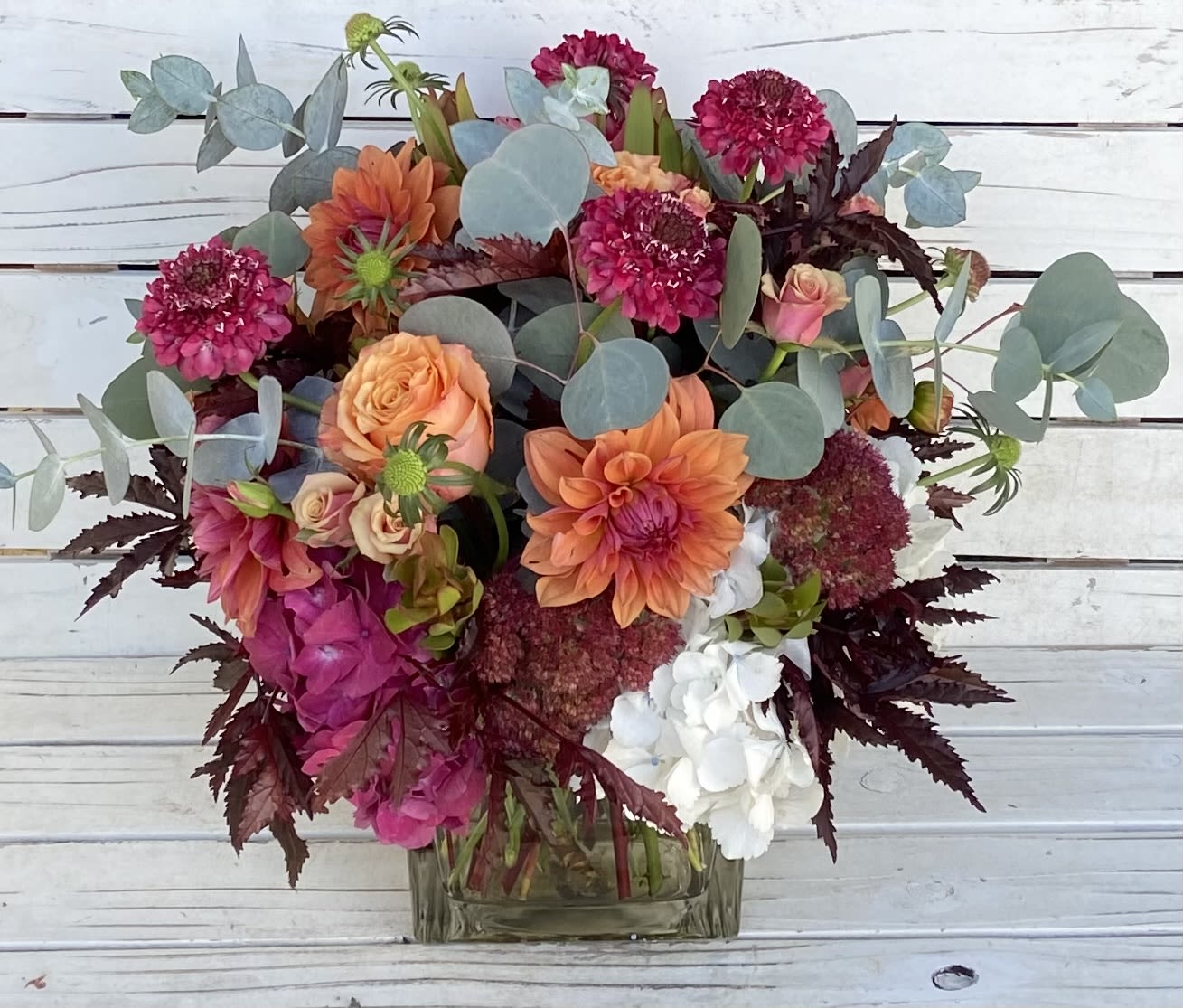 Mixed bouquet of orange, pink, and white flowers in a glass vase