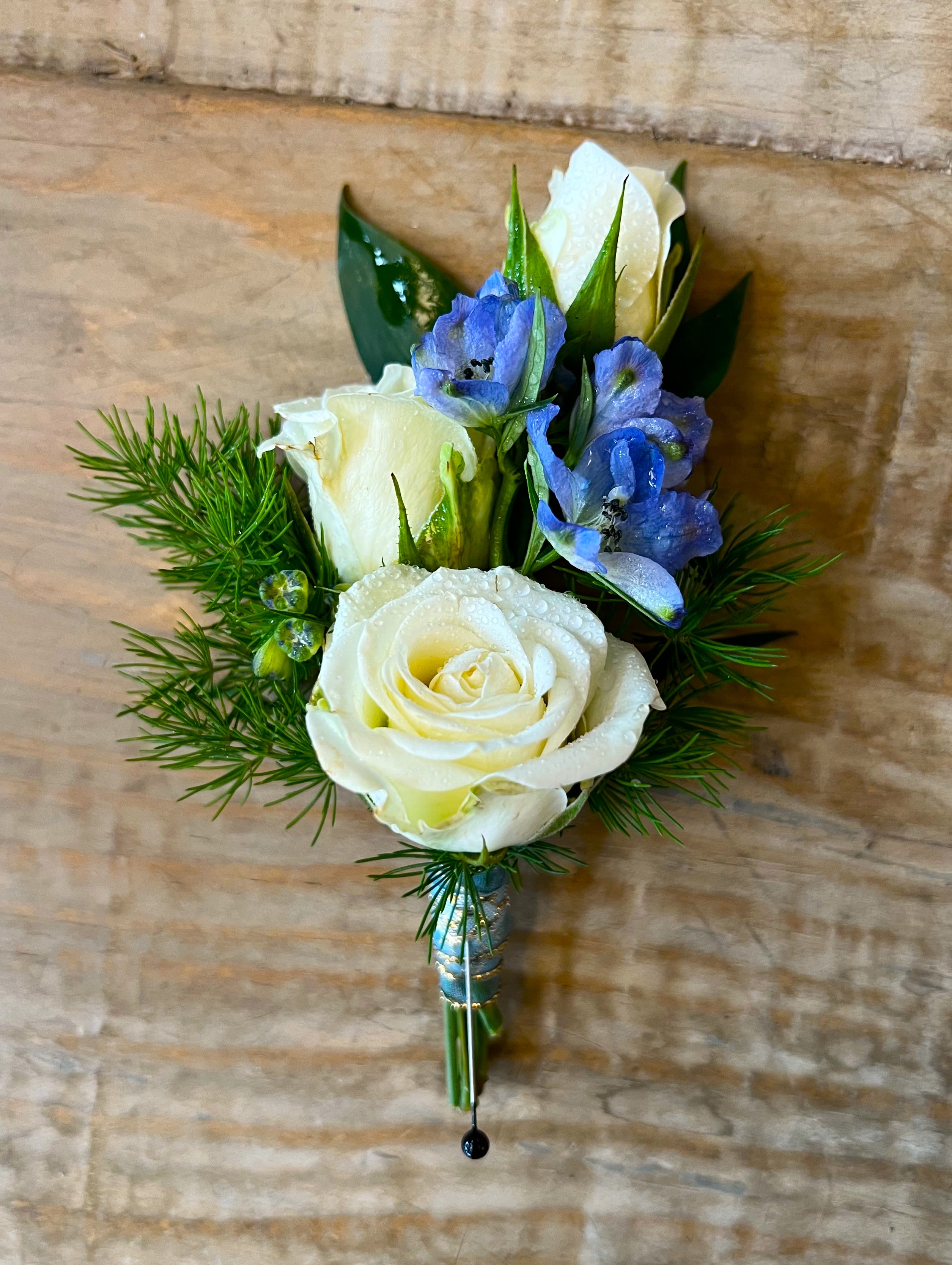 White rose boutonniere with blue flowers and greenery