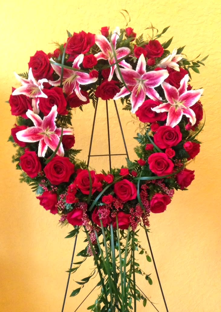 Heart-shaped wreath of red roses and pink lilies on a stand