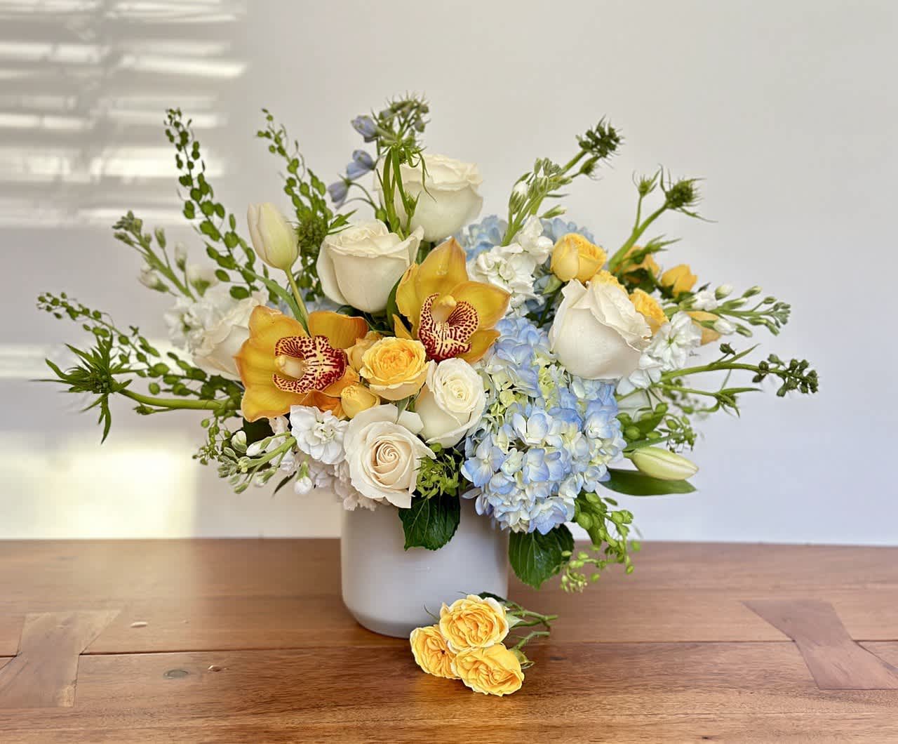 Bouquet of white roses, blue hydrangeas, and yellow orchids in a white vase