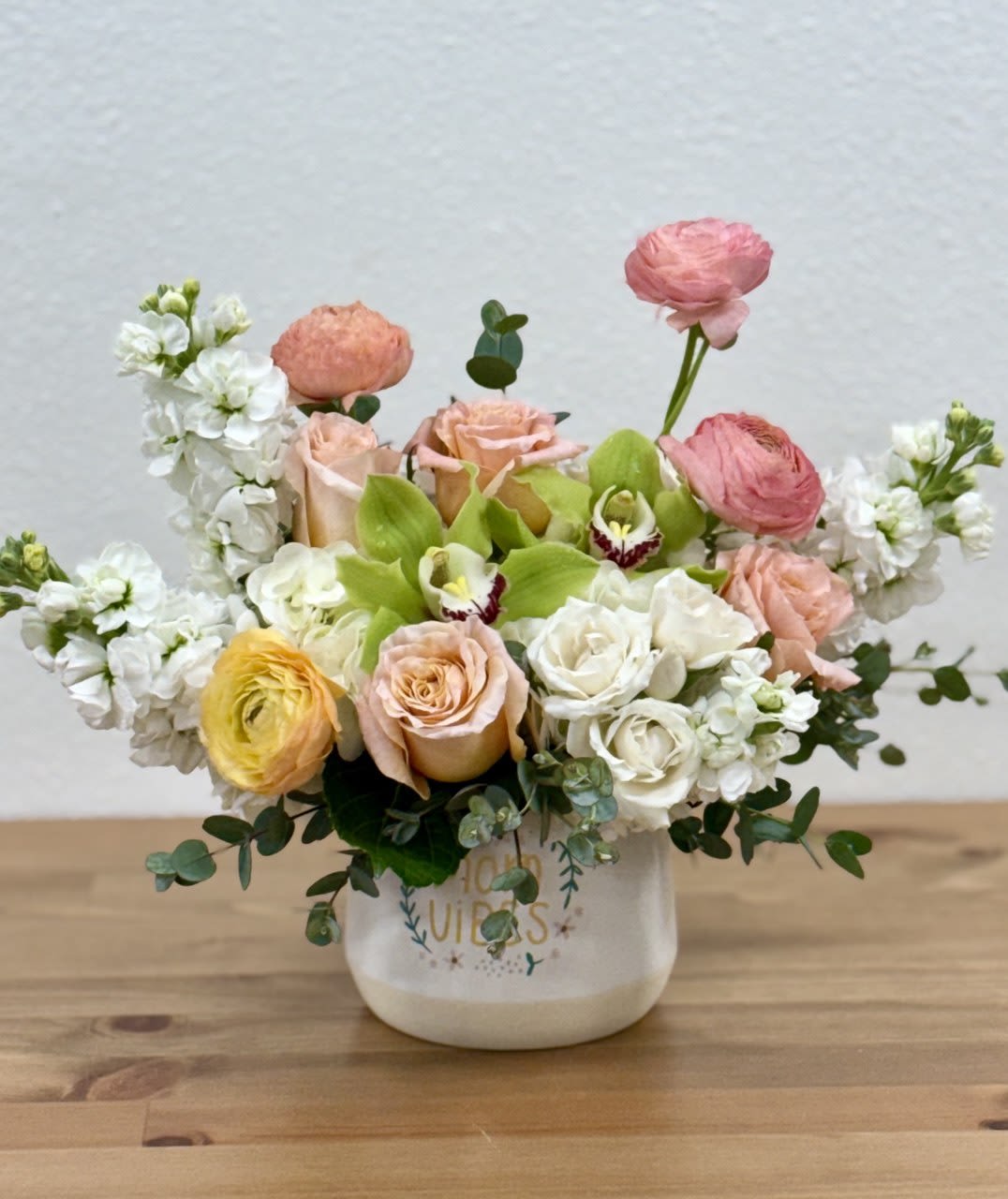 Mixed bouquet of pastel roses, ranunculus, and white blooms in a ceramic vase