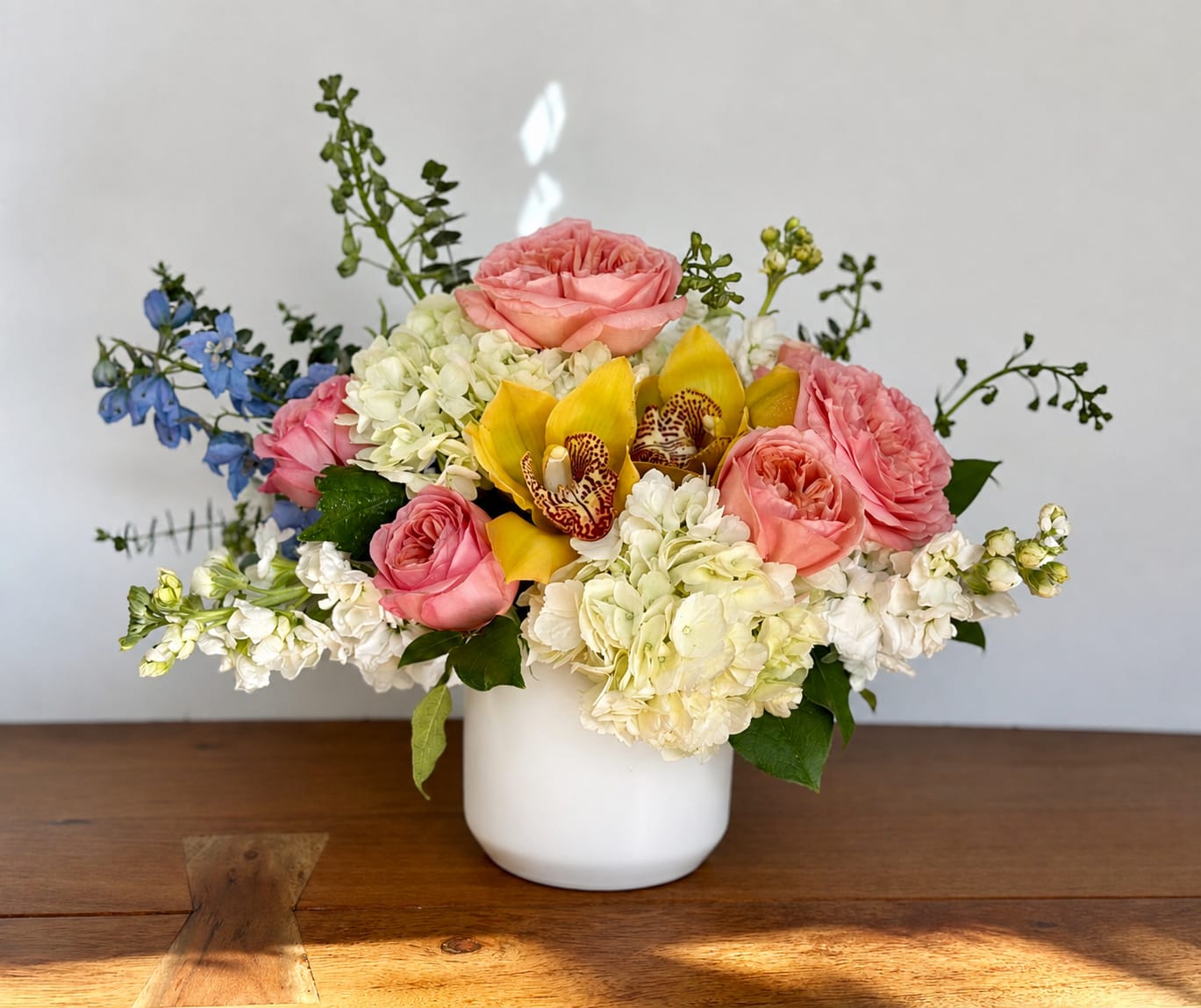 Pink roses, white hydrangeas, and yellow orchids in a white vase