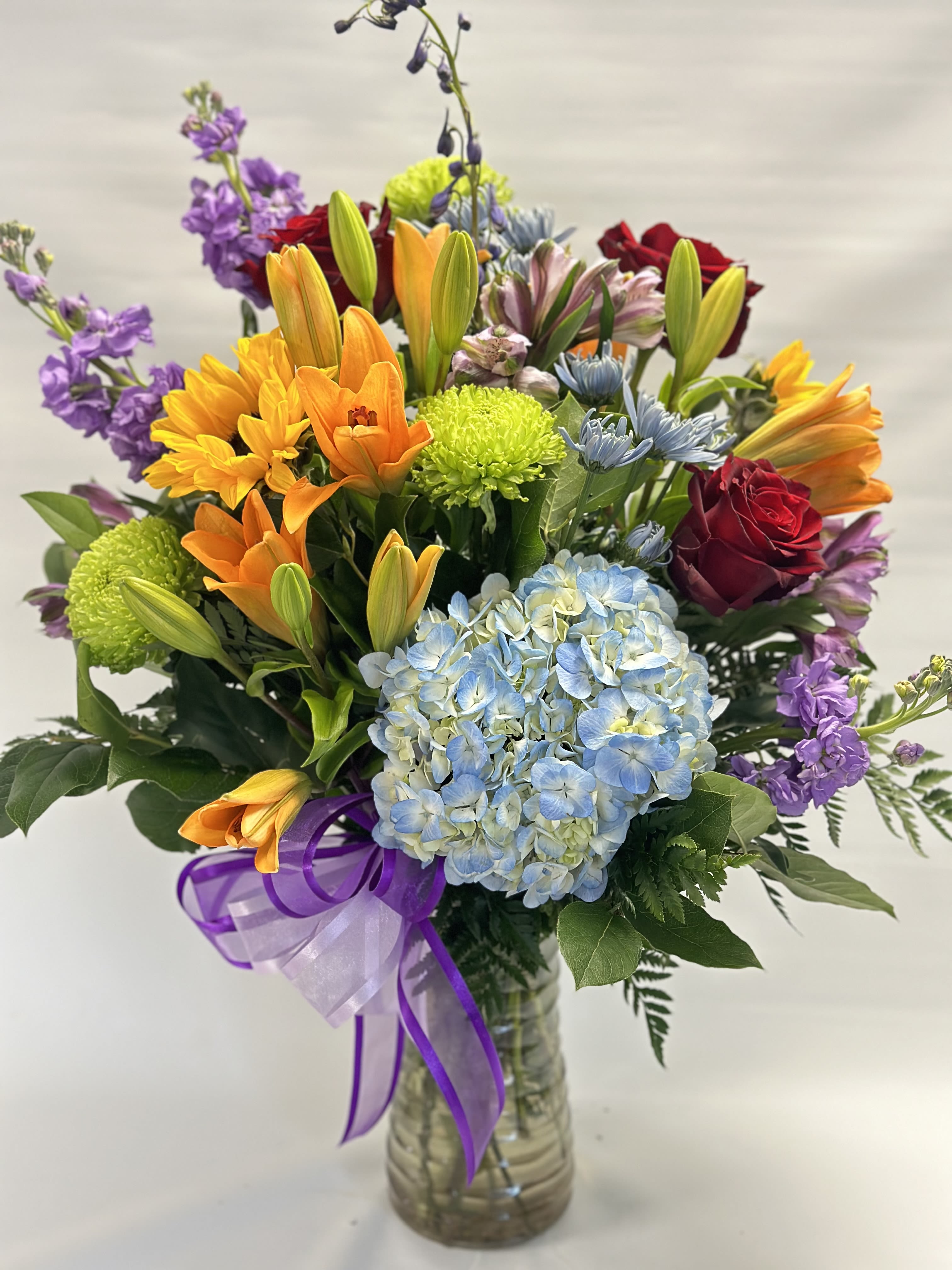 Mixed bouquet in a glass vase with blue hydrangea, roses, lilies, and purple flowers