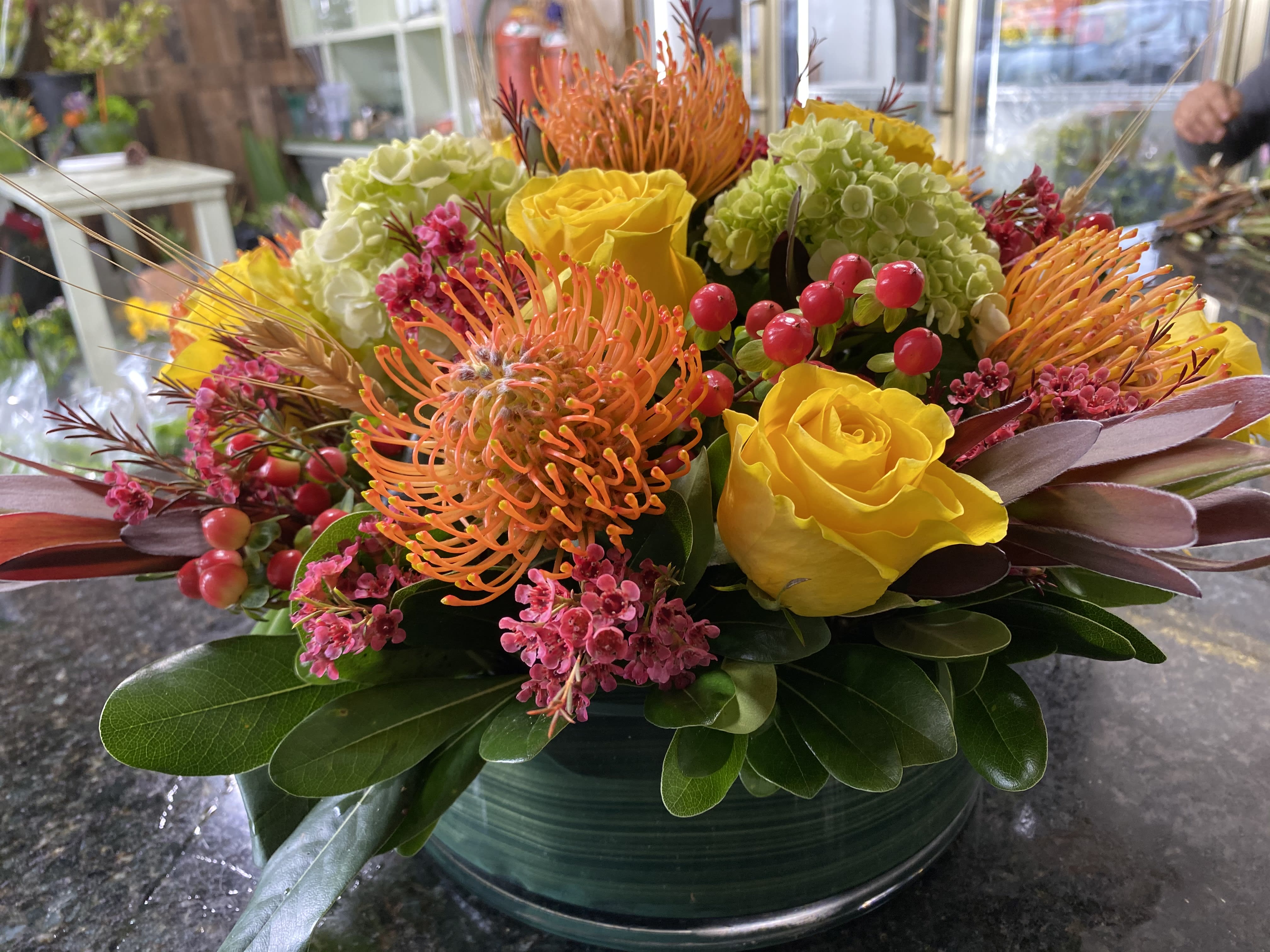  Large Round Table Centerpiece  - Round  Centerpiece **For thanksgiving, we suggest requesting for delivery on 25th to give the flowers time to open. Arranged in a LOW 10 inch diameter round Glass container, Lined.  With all the colors of fall :- Protea / Roses / Hypericum / perfect round centerpiece Height in total about 9 inches and overall about 12-14 inches wide including flowers