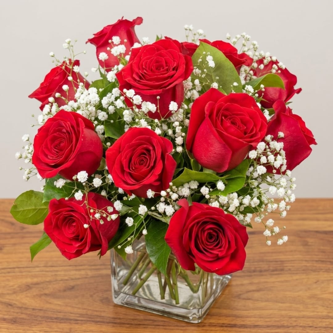 Red roses arranged in a clear square vase with white filler flowers