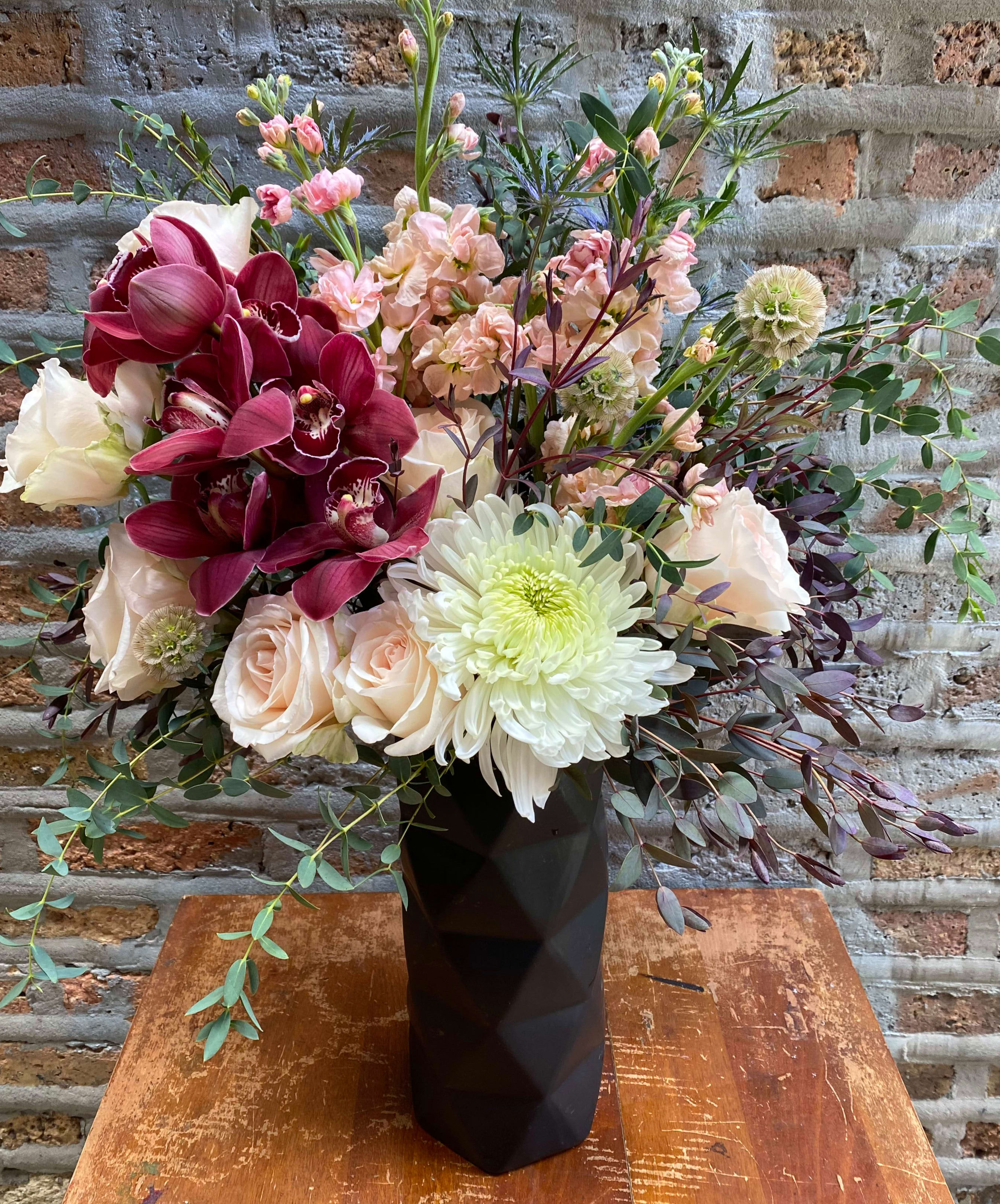 Mixed bouquet in a black vase with burgundy orchids and pale roses