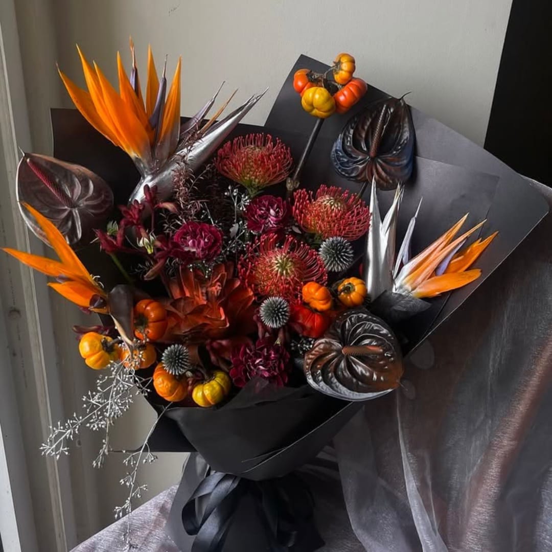 Bouquet with orange bird-of-paradise and dark tropical blooms wrapped in black paper