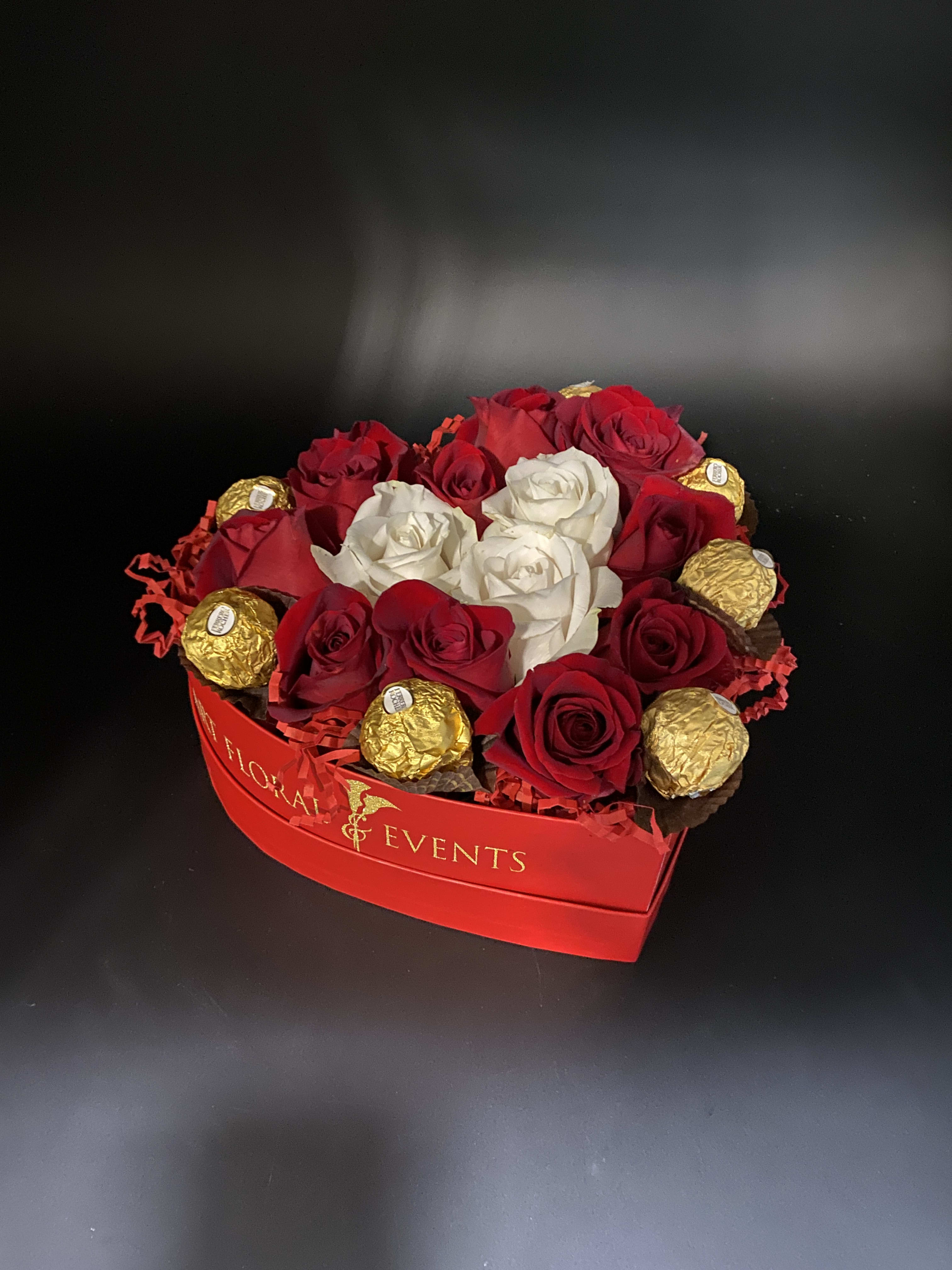 Red and white roses arranged with gold-wrapped chocolates in a red box