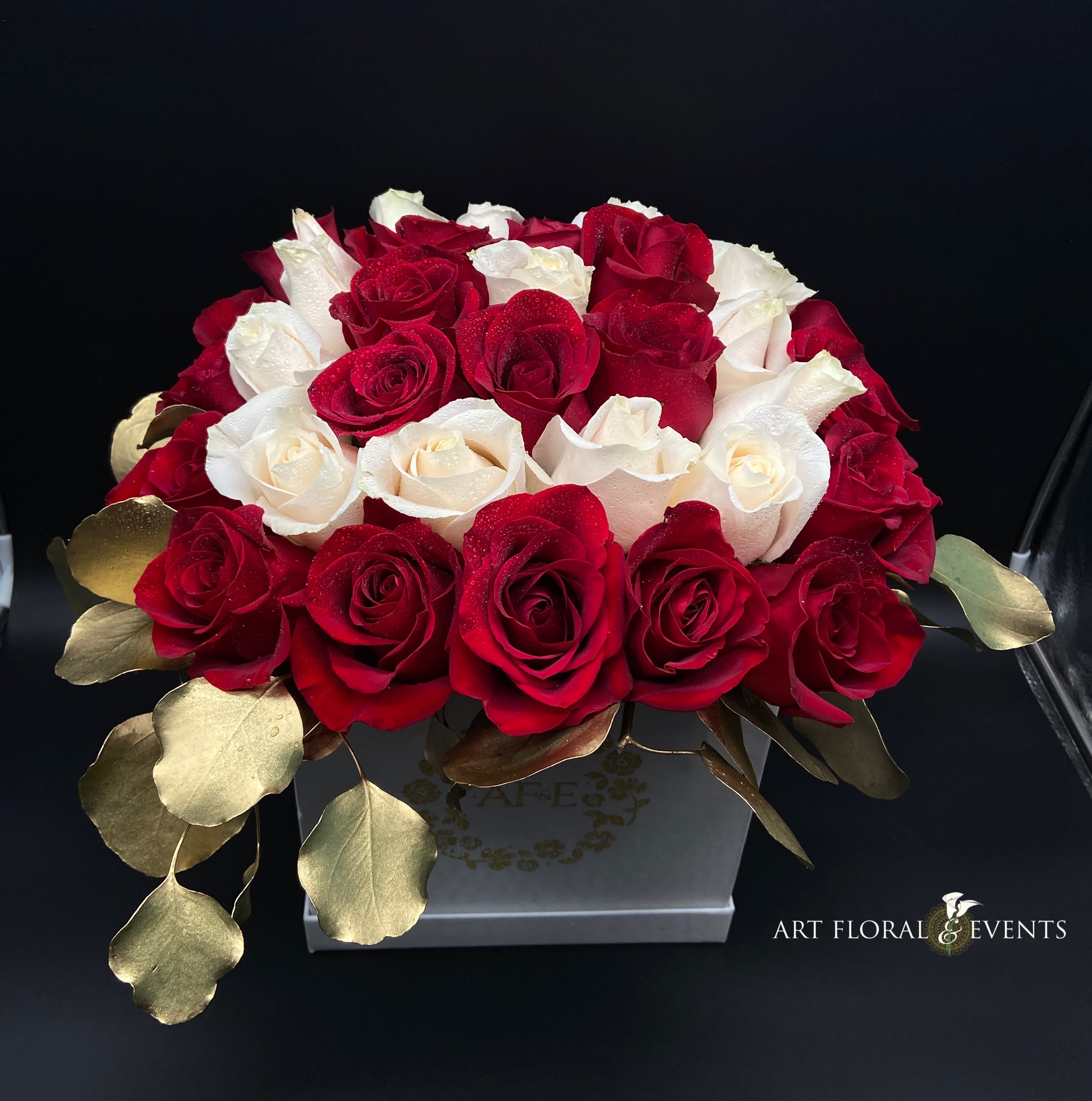 Red and white roses arranged in a square box with gold leaves