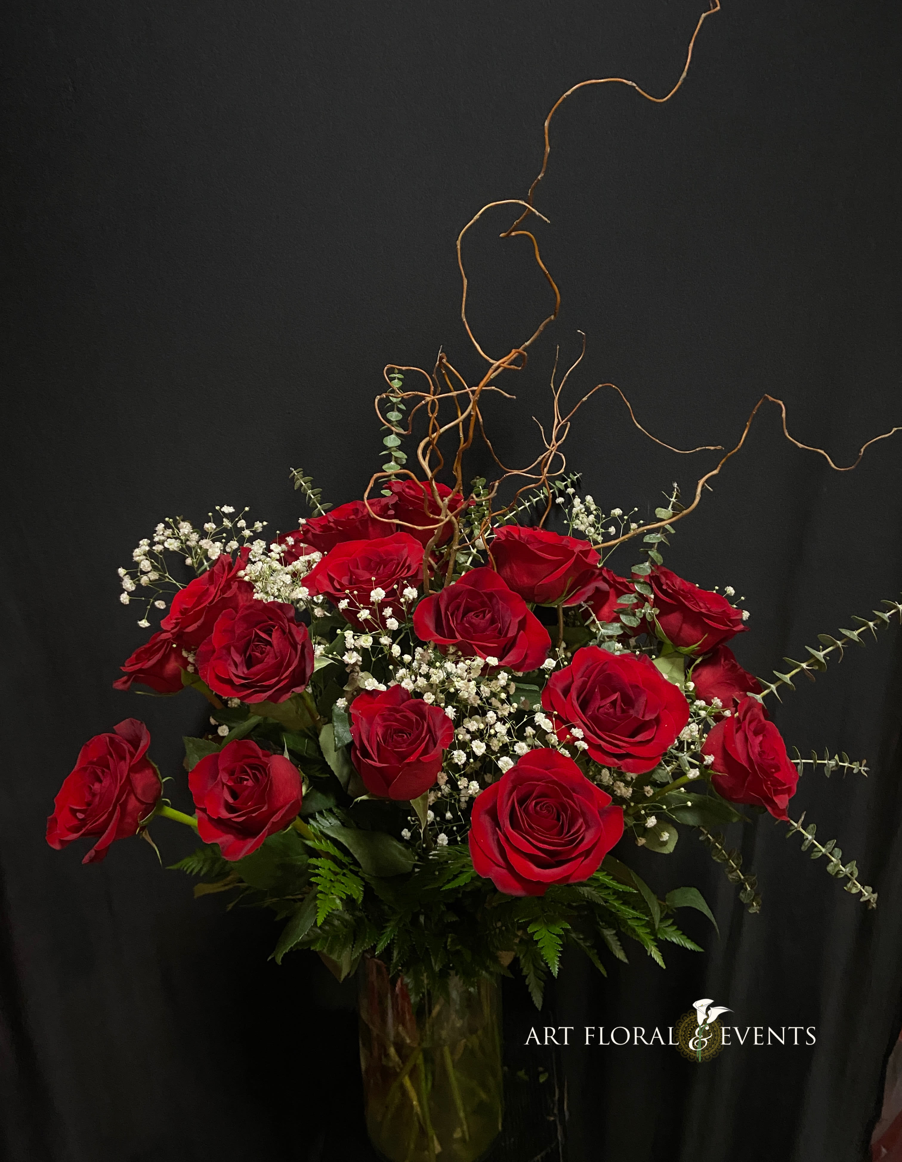Red roses arranged in a tall glass vase with white baby's breath