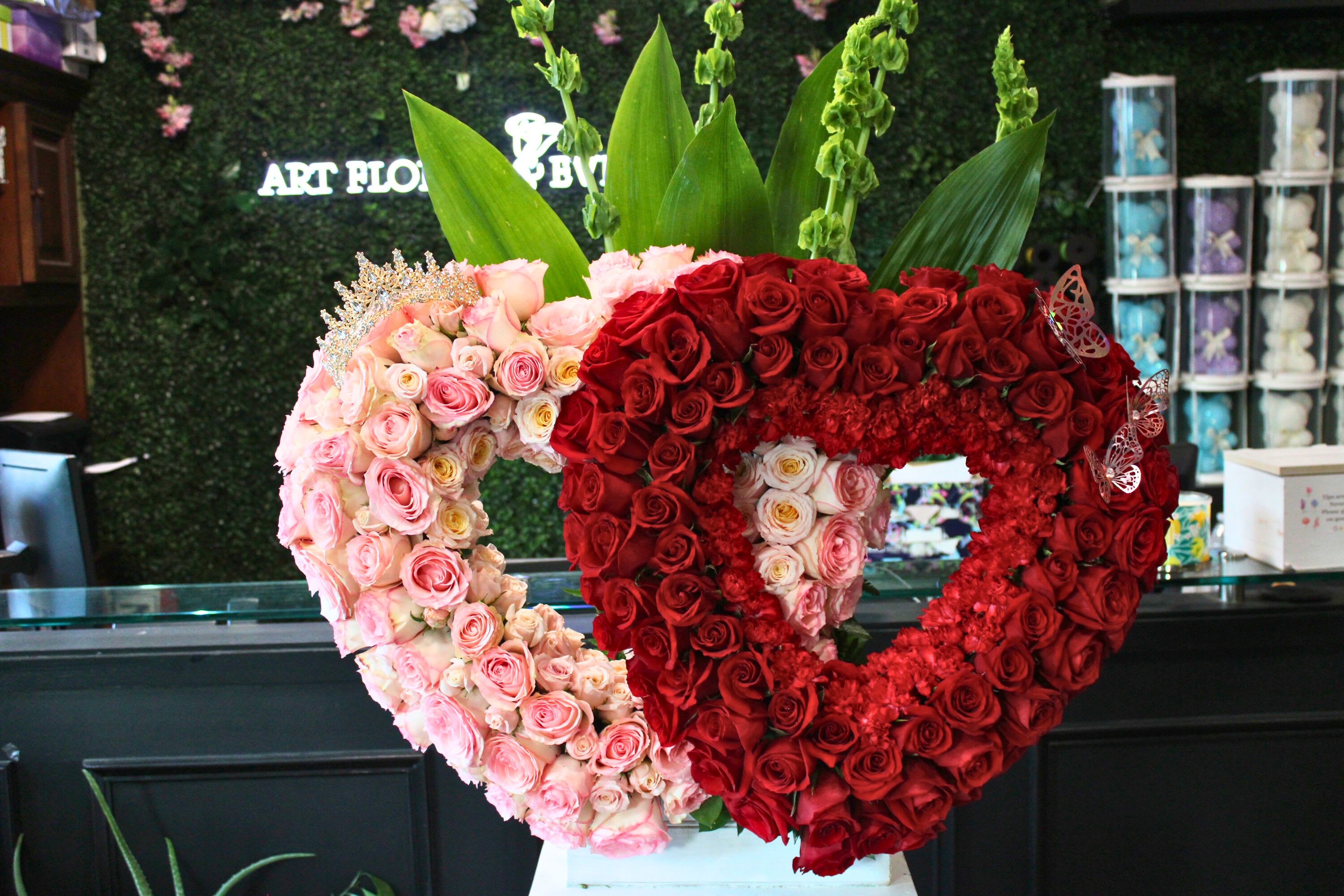 Heart-shaped rose arrangements in pink and red with tall green leaves behind them