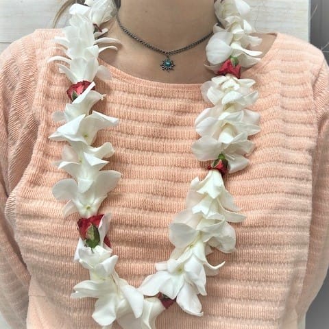 White flower lei with red accents worn over a peach sweater