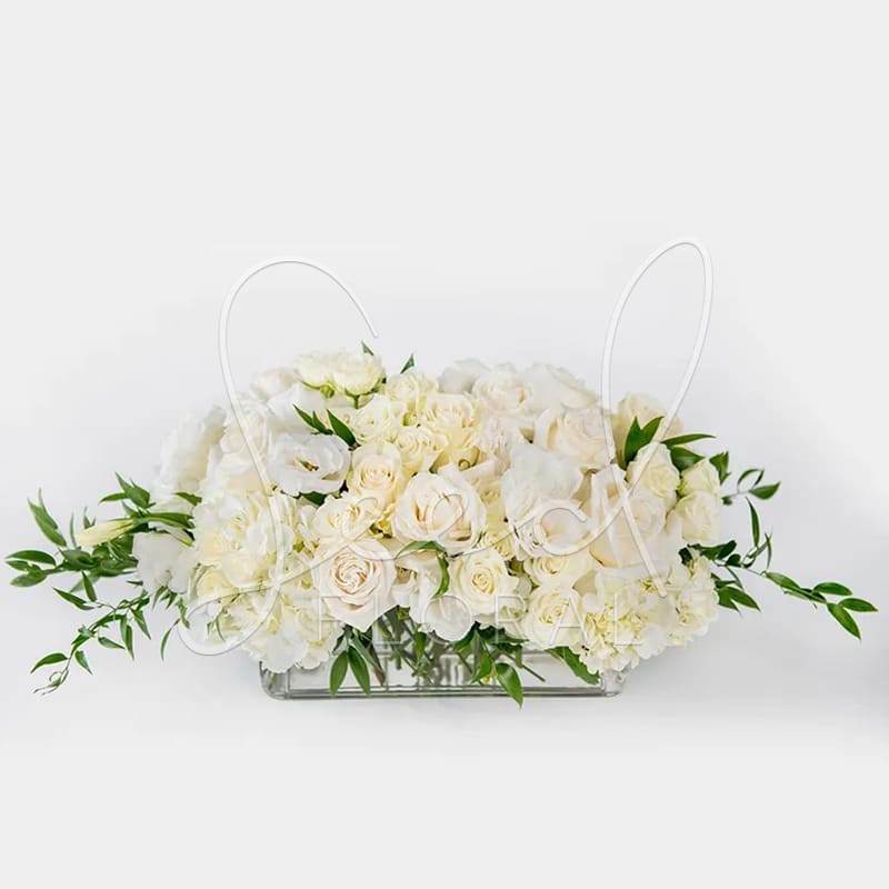 Low rectangular centerpiece of ivory roses and white blooms in a clear glass vase
