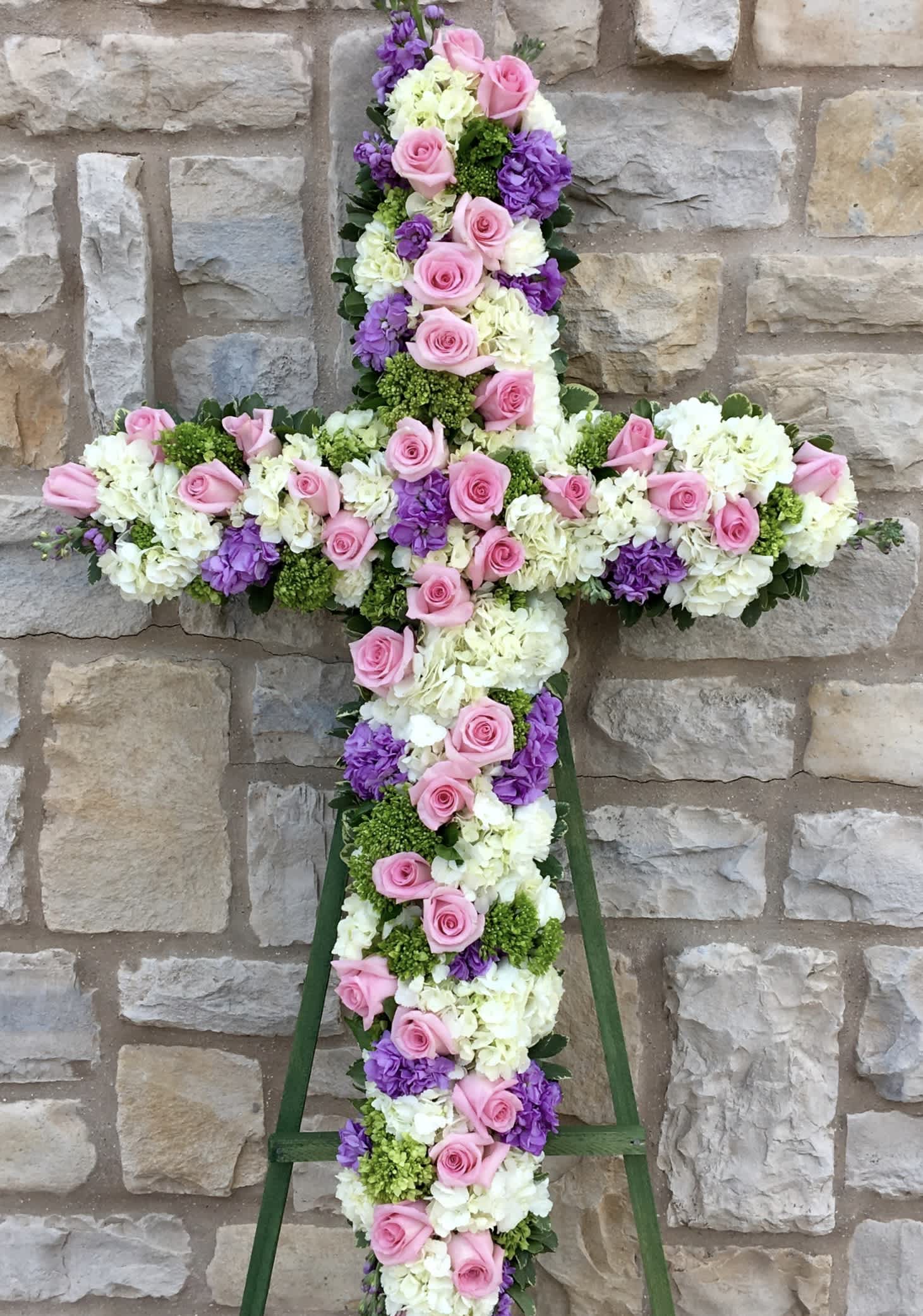 Floral cross arrangement with pink roses, white hydrangeas, and purple blooms