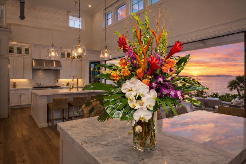 Tall tropical bouquet with white orchids and red-orange flowers in a glass vase