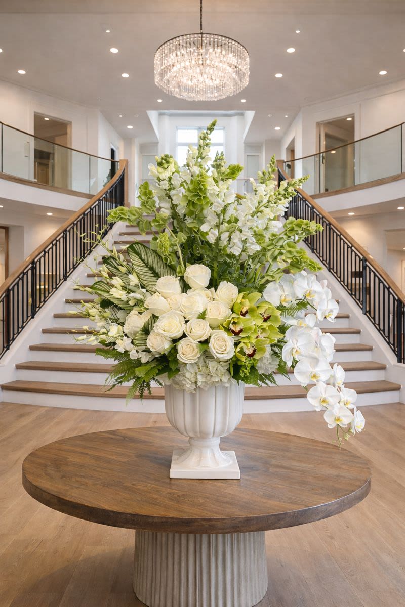 Large white floral arrangement in a pedestal vase with cascading orchids