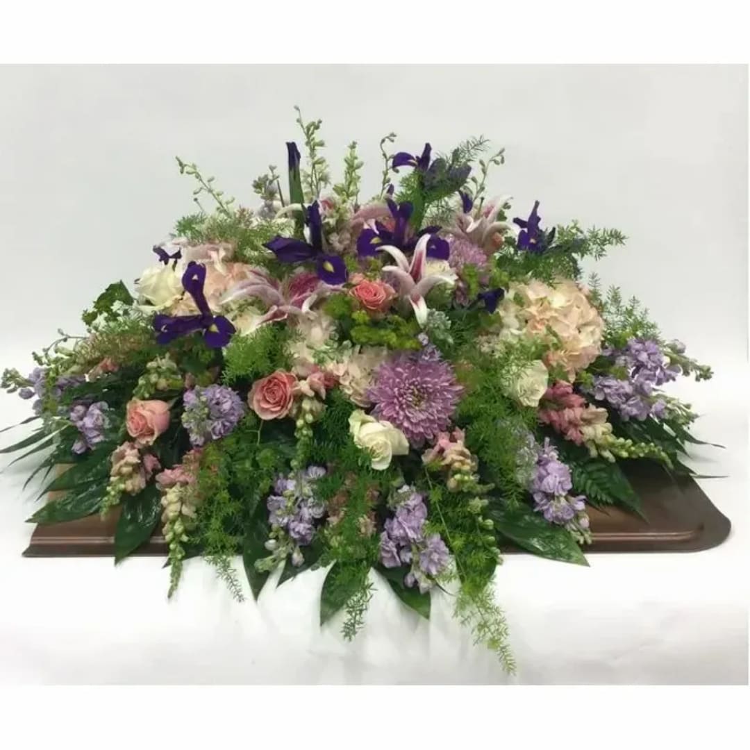 Large mixed floral arrangement with purple, pink, and white blooms on a casket