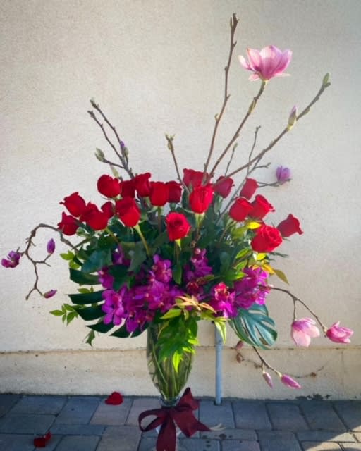 Tall bouquet of red roses and pink magnolia blossoms in a glass vase