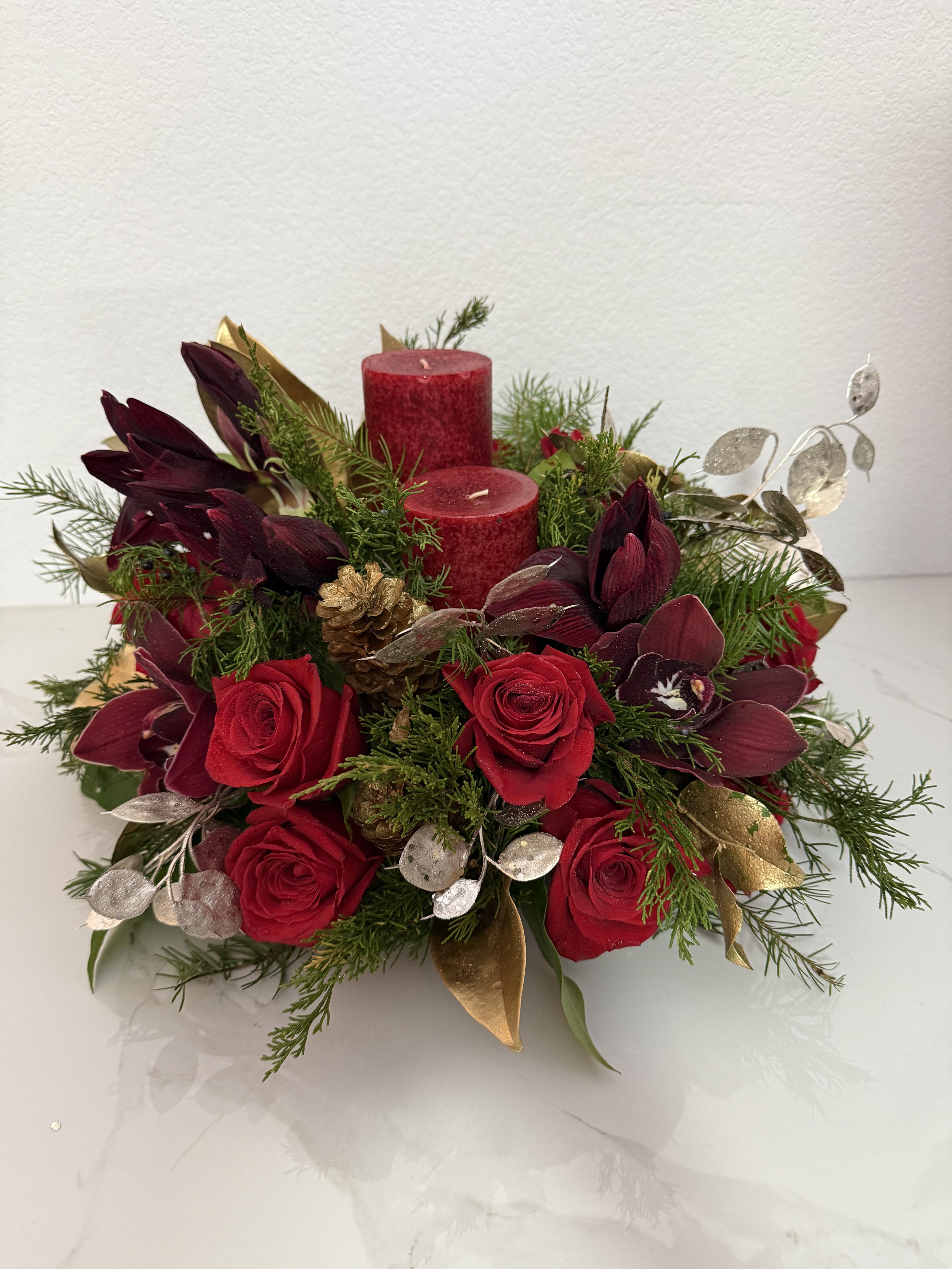 Red roses and burgundy orchids arranged with candles and greenery