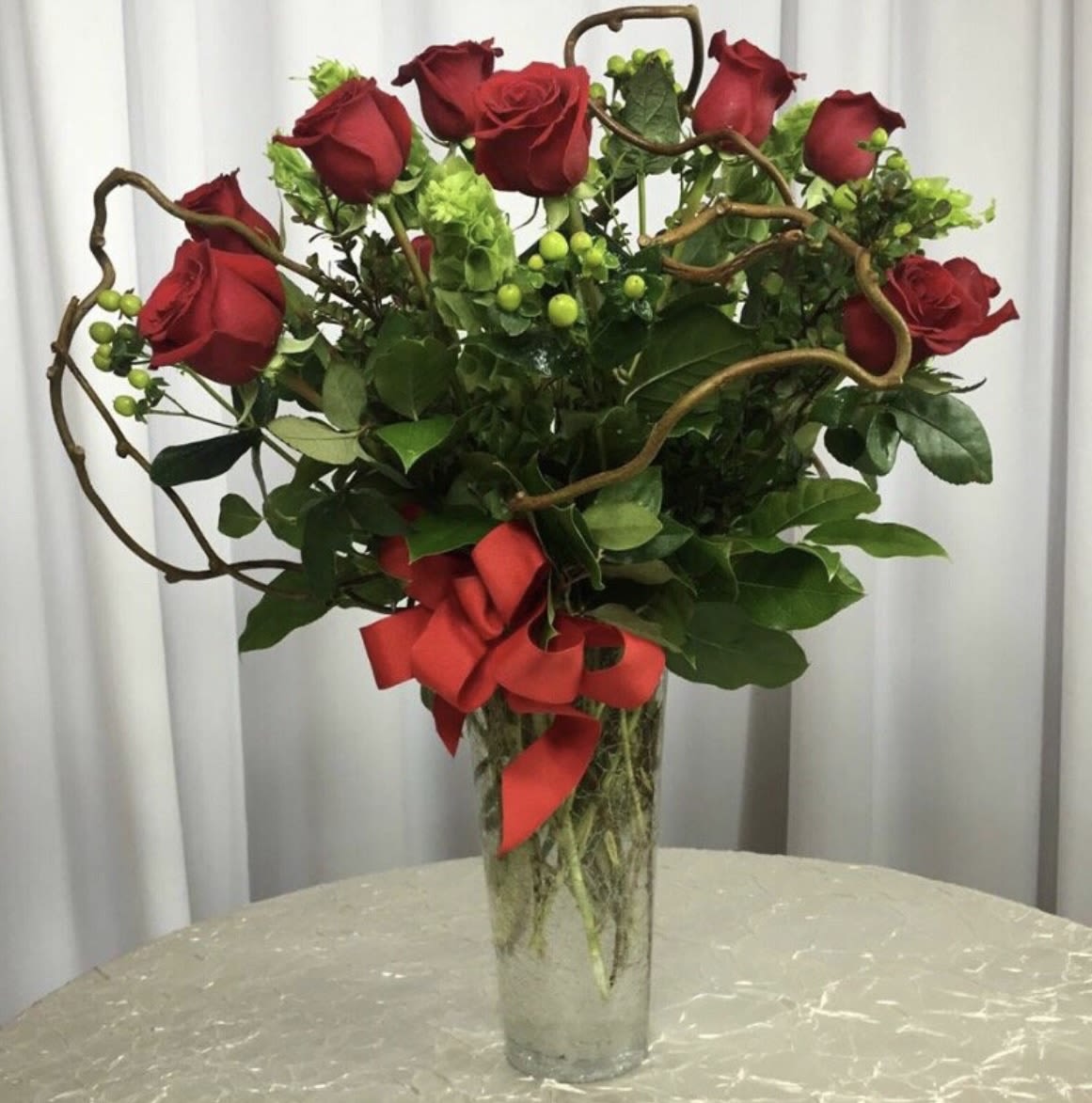 Red roses in a tall glass vase with a red ribbon