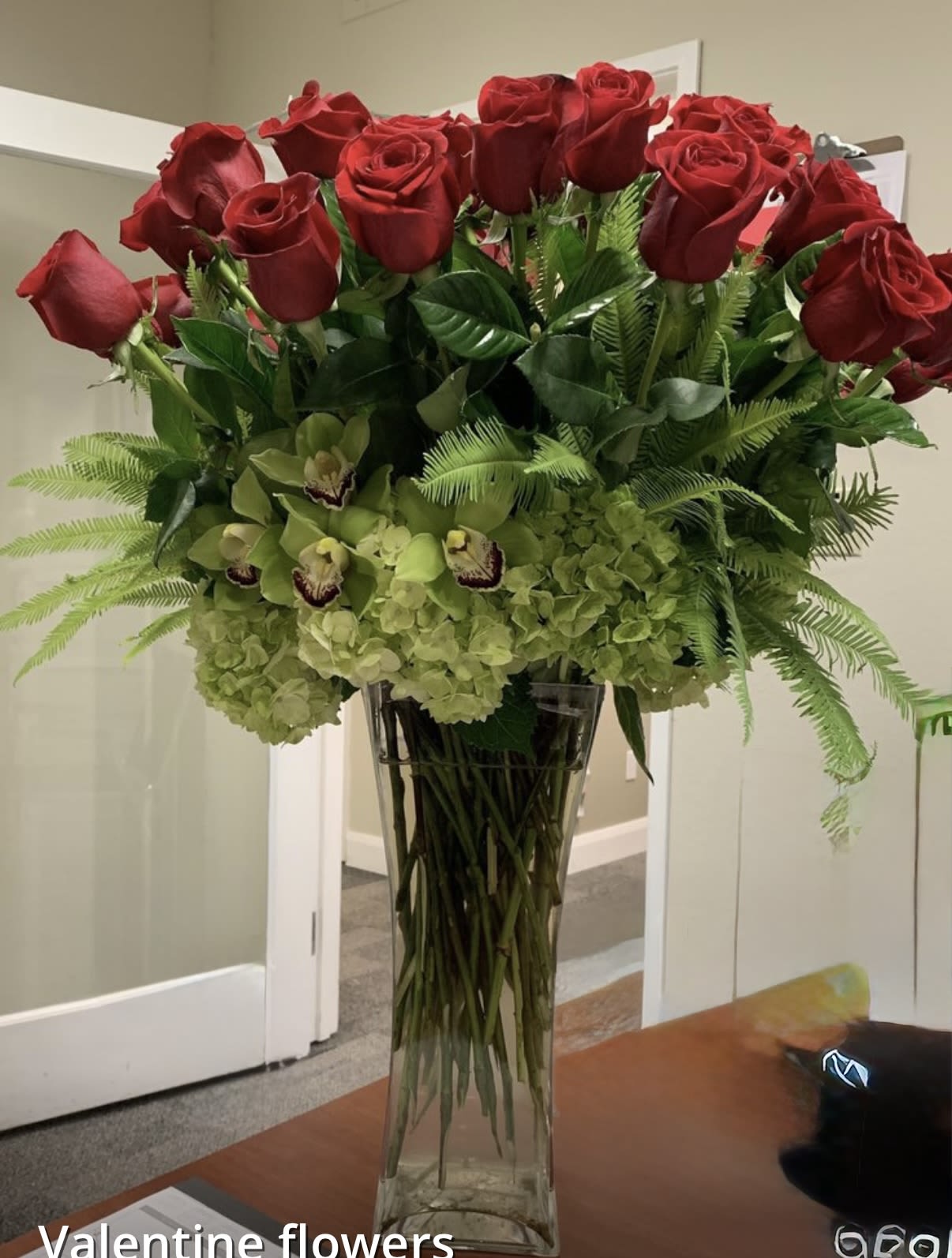 Tall vase arrangement of red roses, green orchids, and hydrangeas