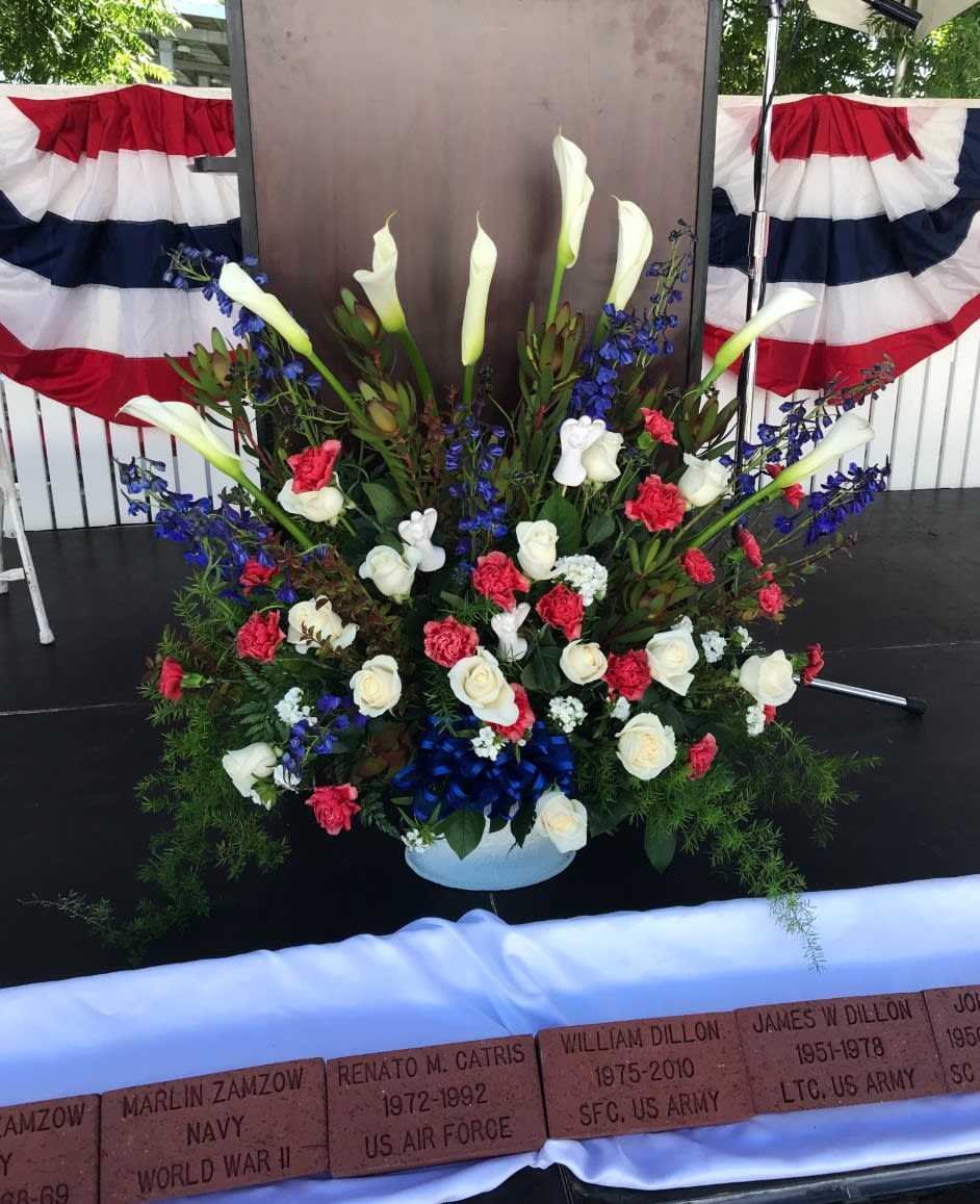 Large memorial floral arrangement with white calla lilies, roses, and blue flowers
