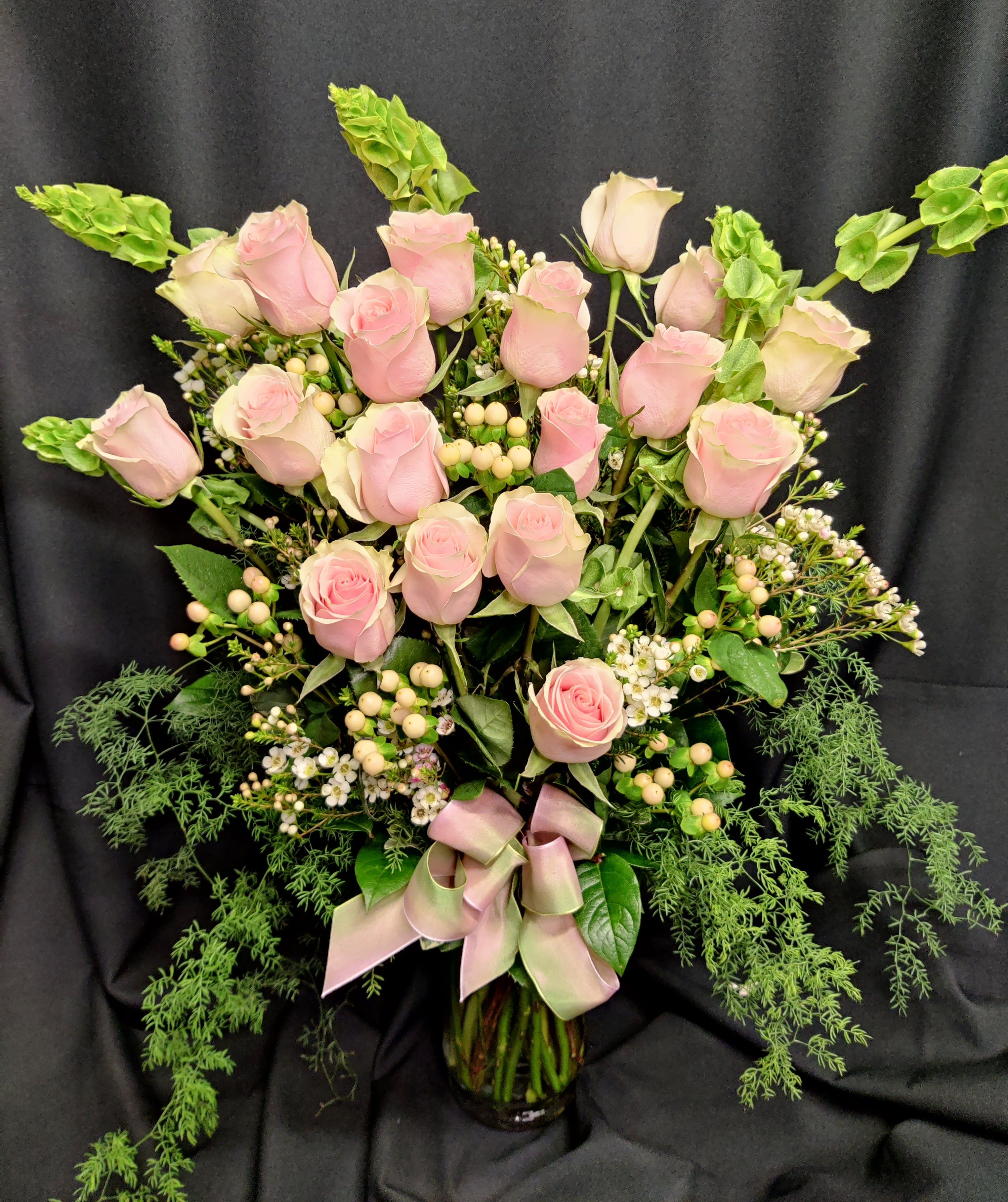 Pink roses arranged in a glass vase with greenery and a pink ribbon
