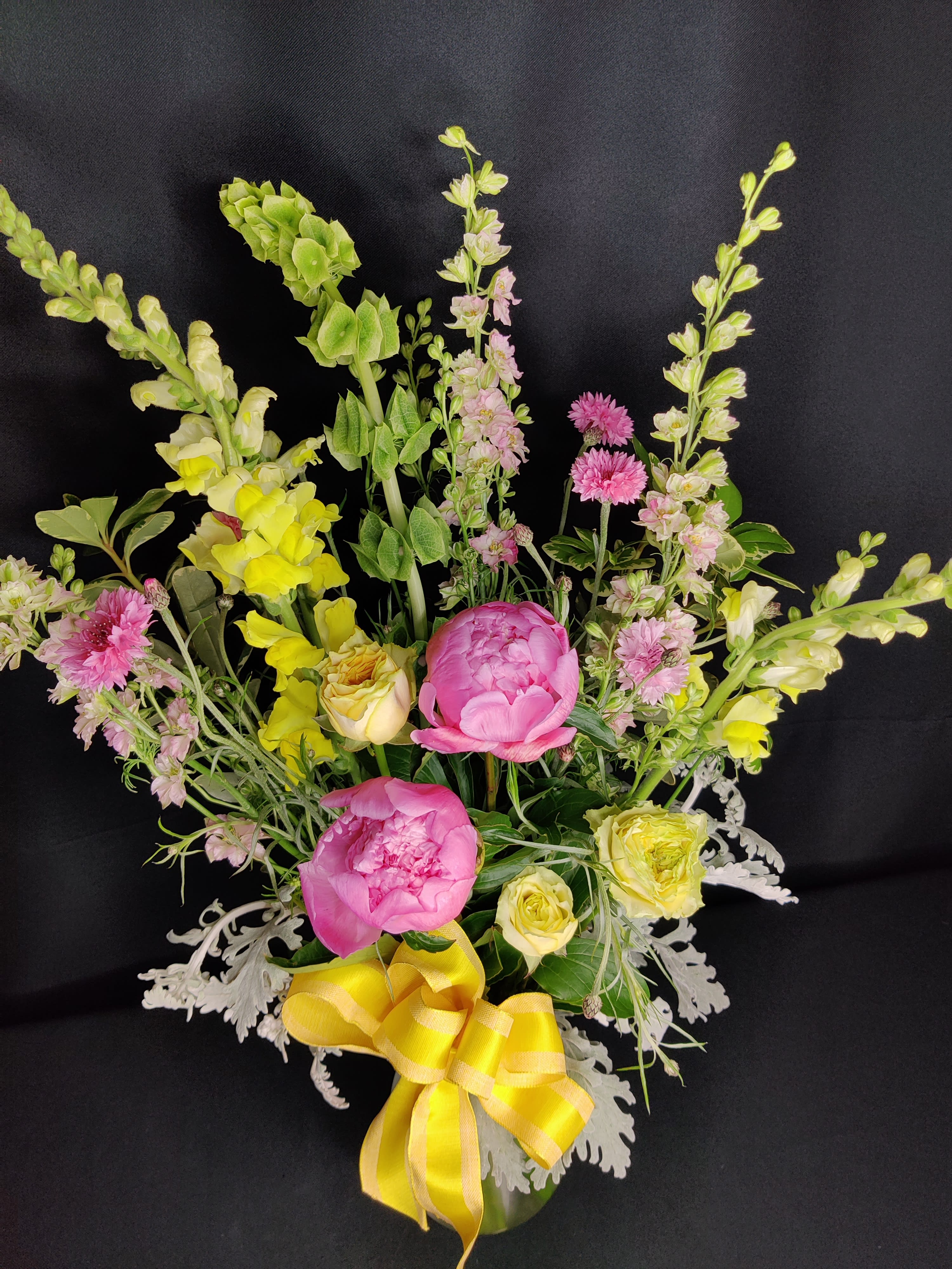Pink peonies and yellow flowers in a vase with a yellow ribbon