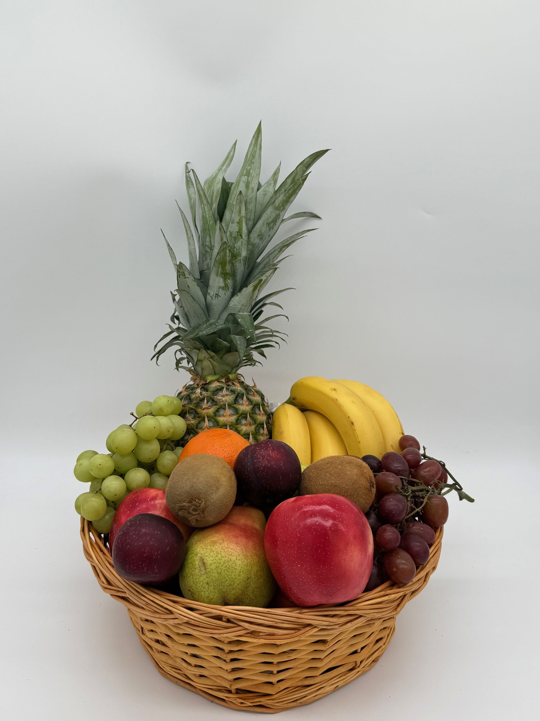 Fruit basket with pineapple, bananas, grapes, kiwi, oranges, apples, and pears