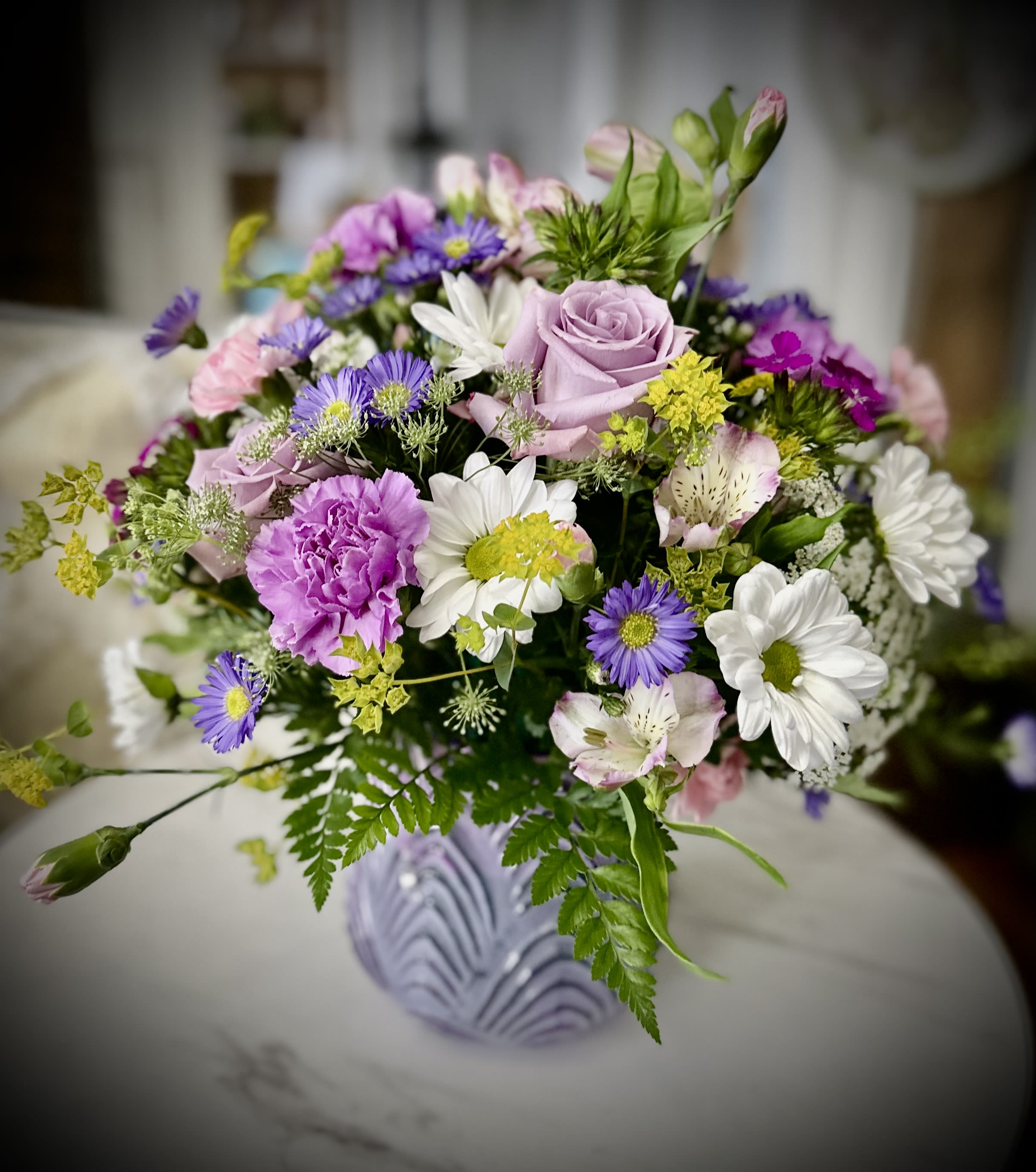 Mixed bouquet of pink, purple, and white flowers in a lavender vase