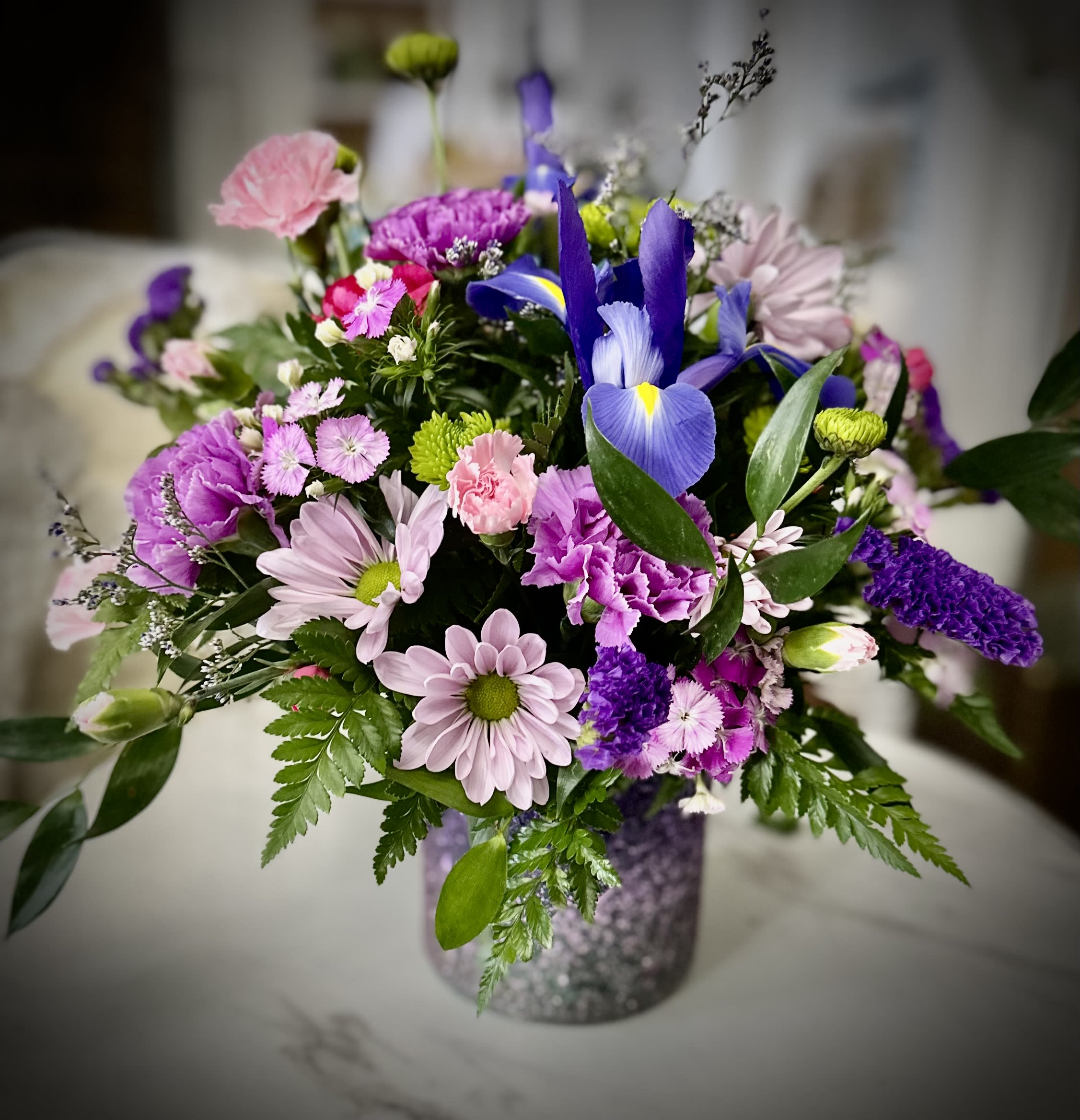 Mixed bouquet of purple, pink, and white flowers in a glittery vase