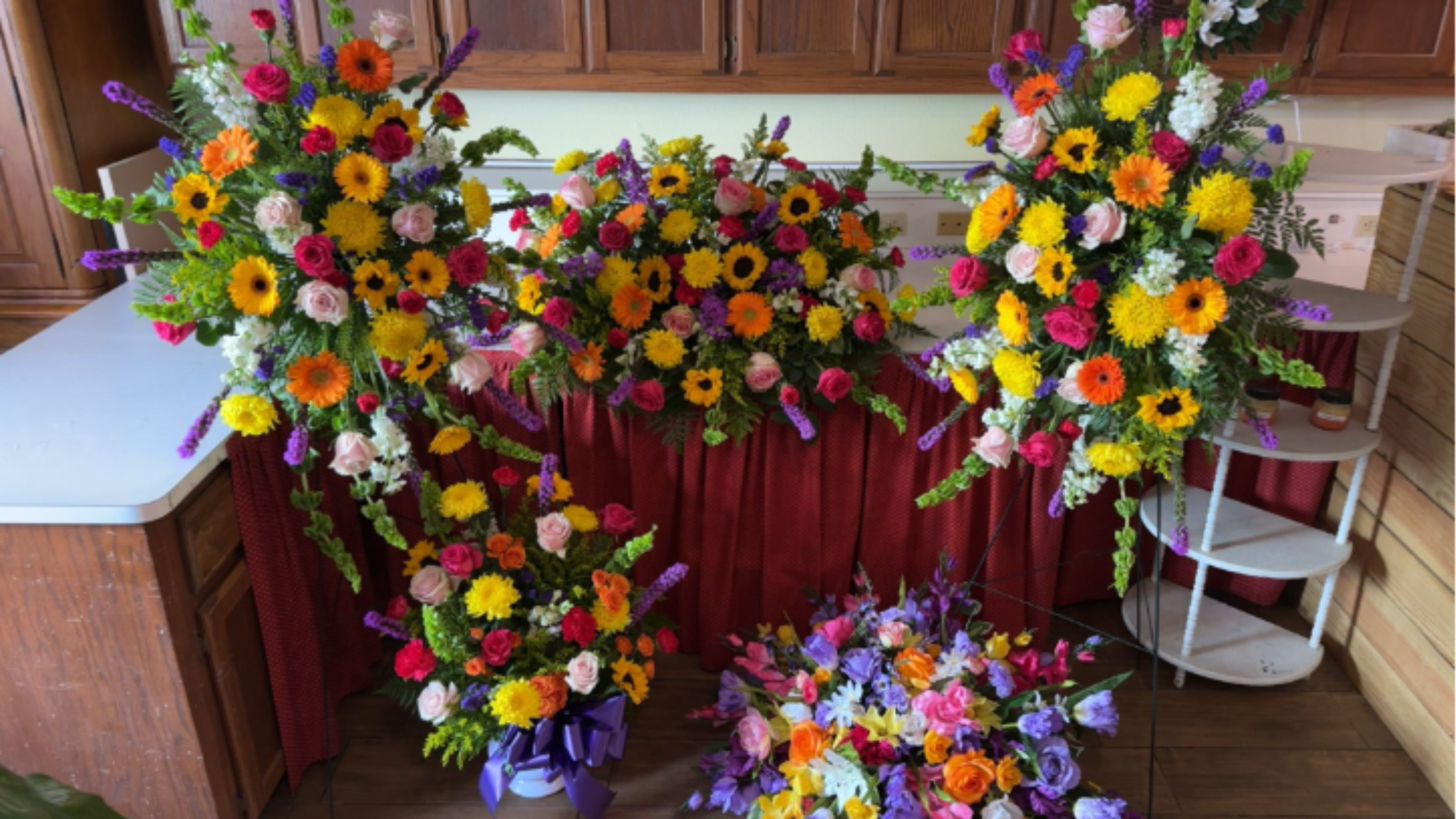 Set of bright mixed funeral sprays and a casket spray with yellow, pink, orange, and purple flowers.
