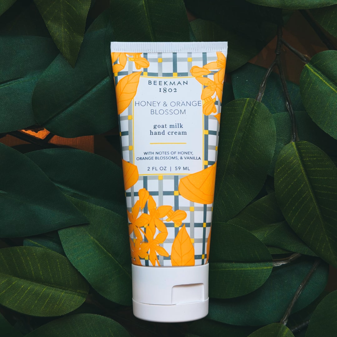 Tube of honey and orange blossom hand cream on dark green leaves