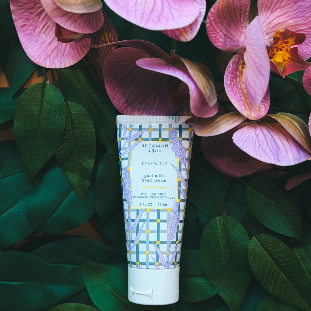 Lavender hand cream tube surrounded by pink orchid blooms and dark green leaves