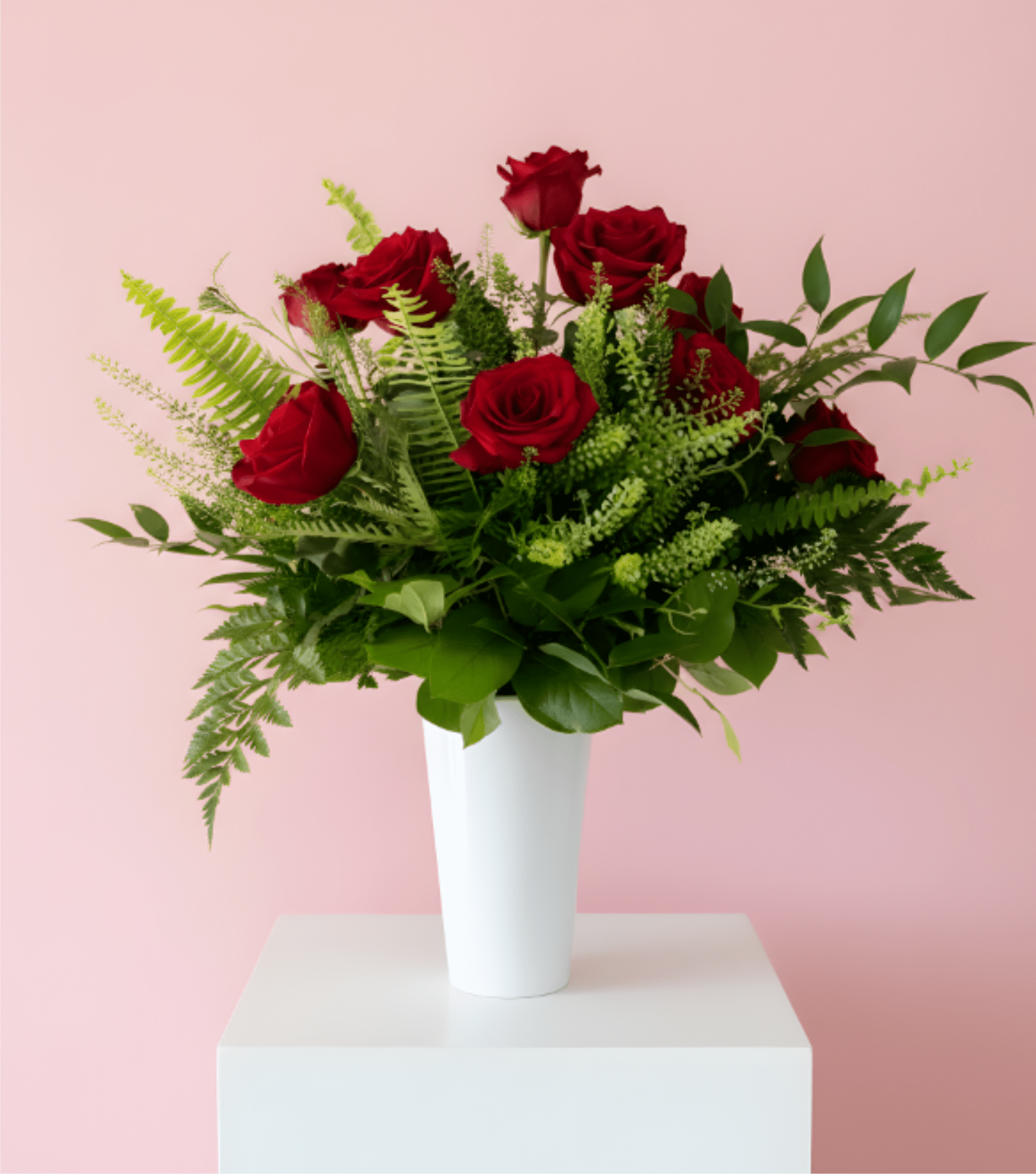 Red roses arranged in a white vase with green foliage