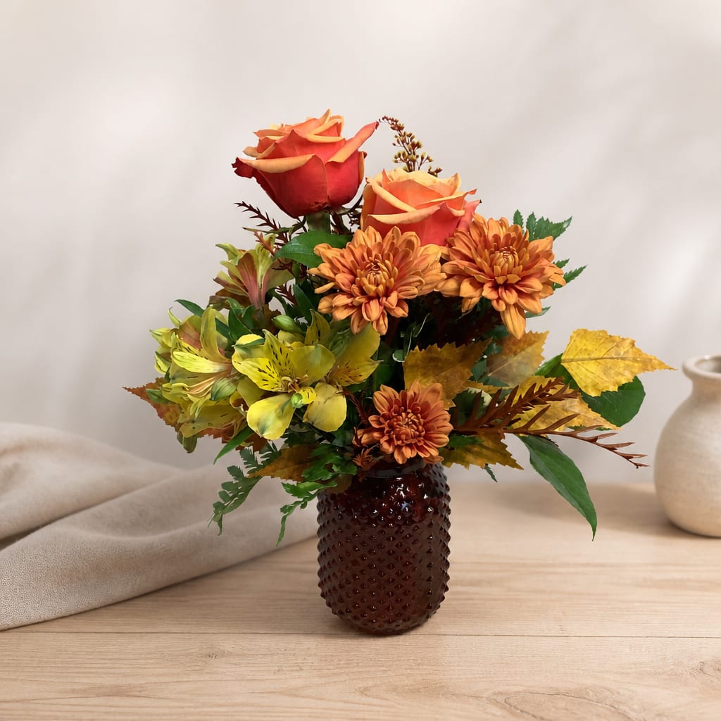 Orange roses and chrysanthemums arranged in a dark vase