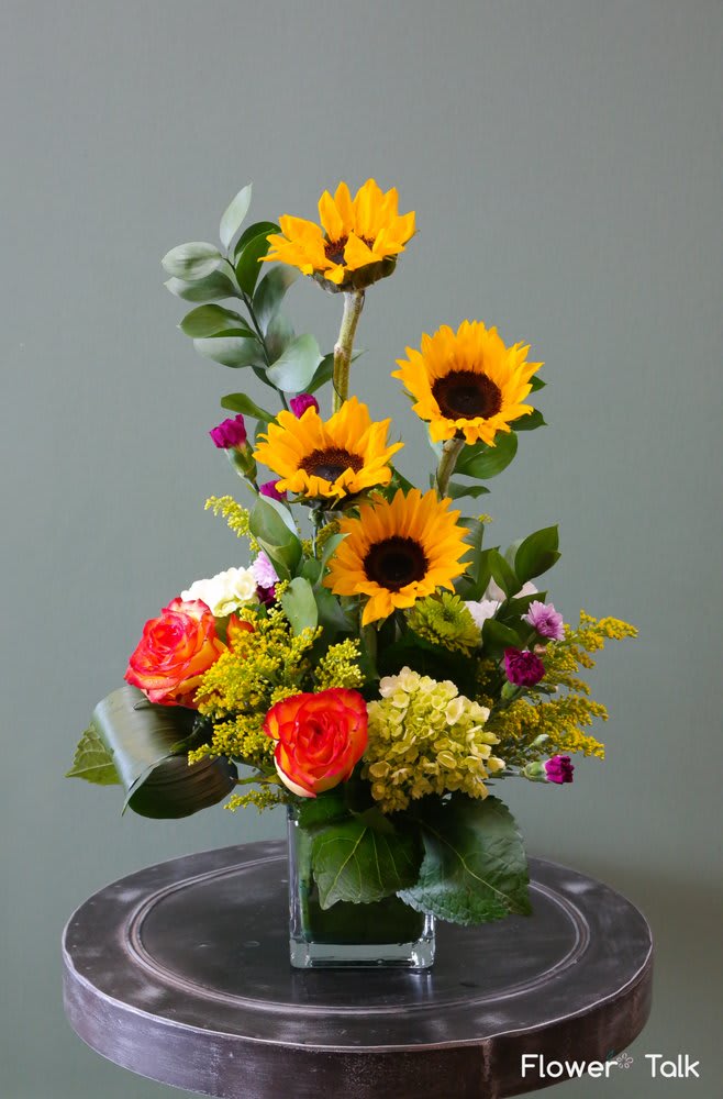 Sunflower and rose arrangement in a square glass vase